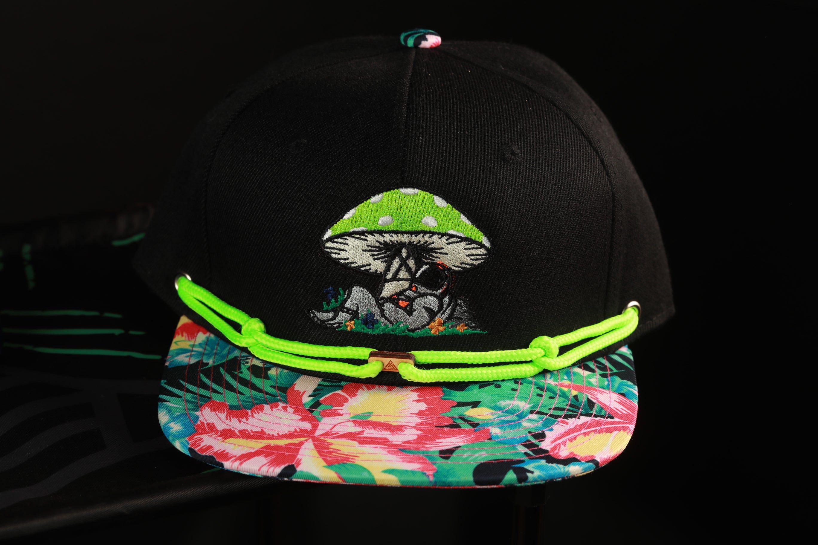 A black baseball cap with a colorful floral pattern and a green mushroom design on the front.