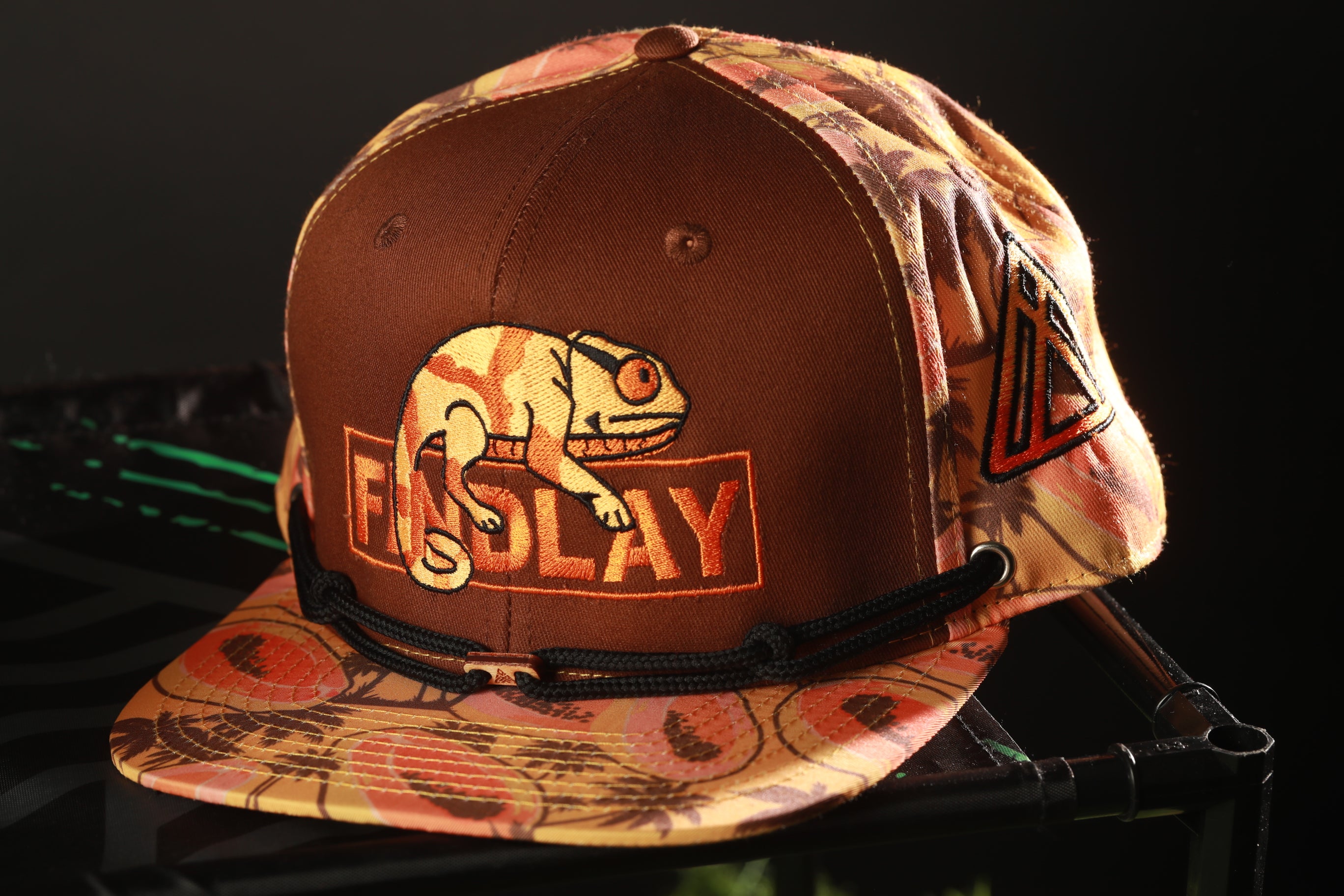 A brown baseball cap with a patterned design and a chameleon graphic on it.