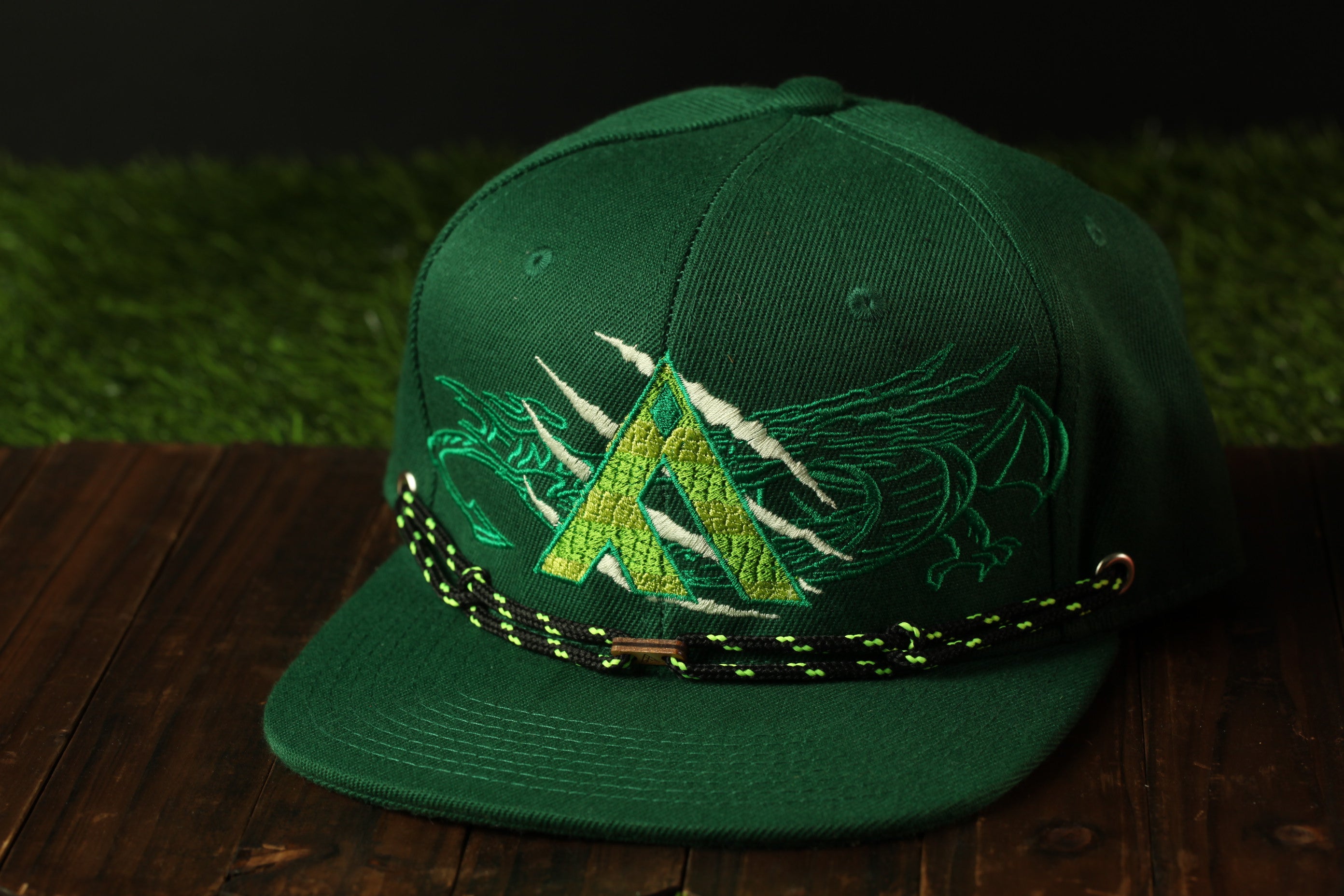 A green baseball cap with a dragon design on it, placed on a wooden surface.