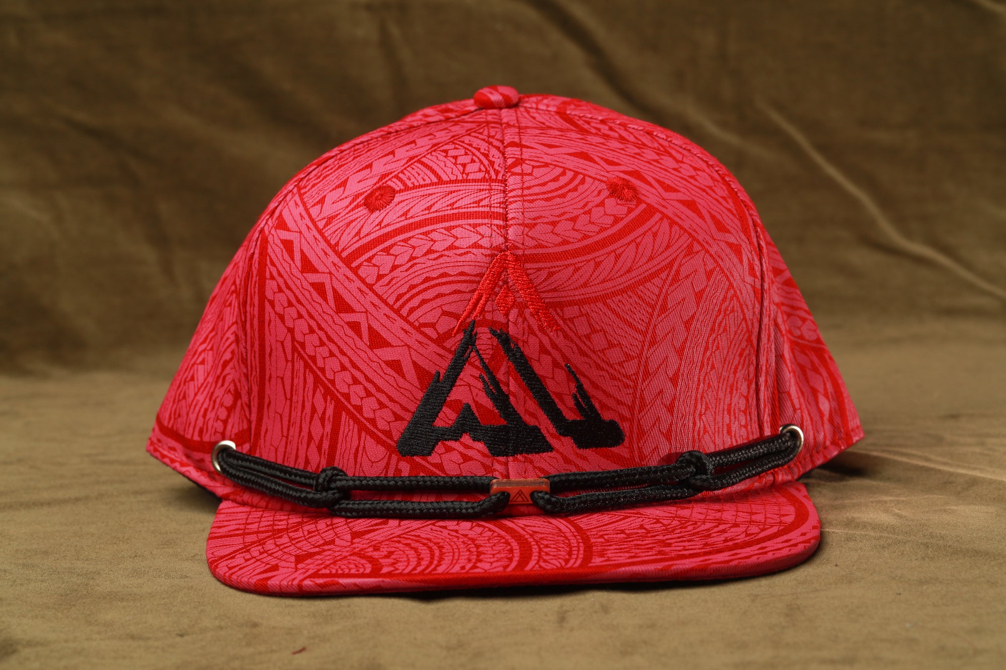 A red baseball cap with a black logo on it, placed on a brown surface.