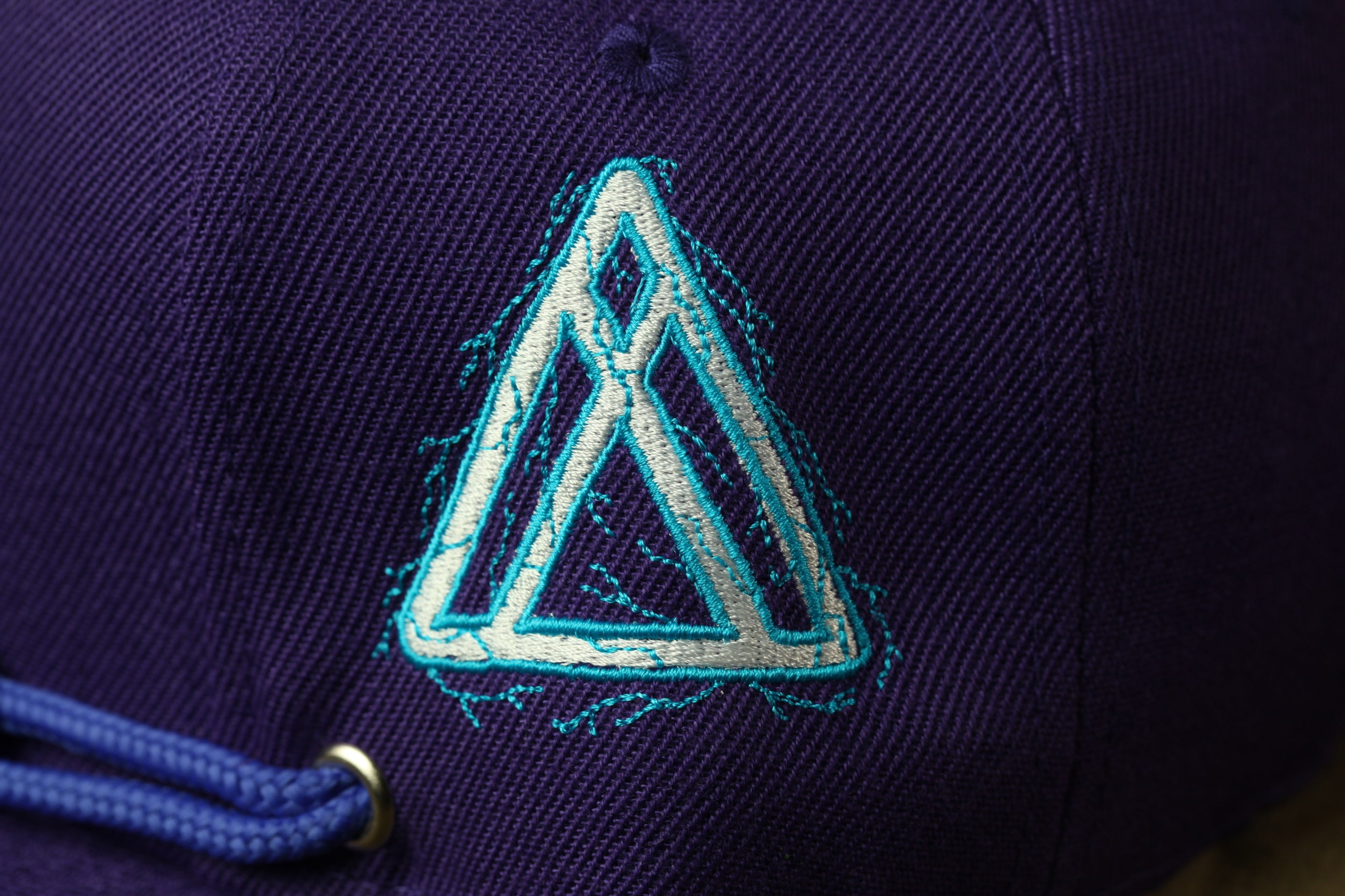 A close-up view of a dark purple fabric with a white triangle-shaped embroidered logo on it.