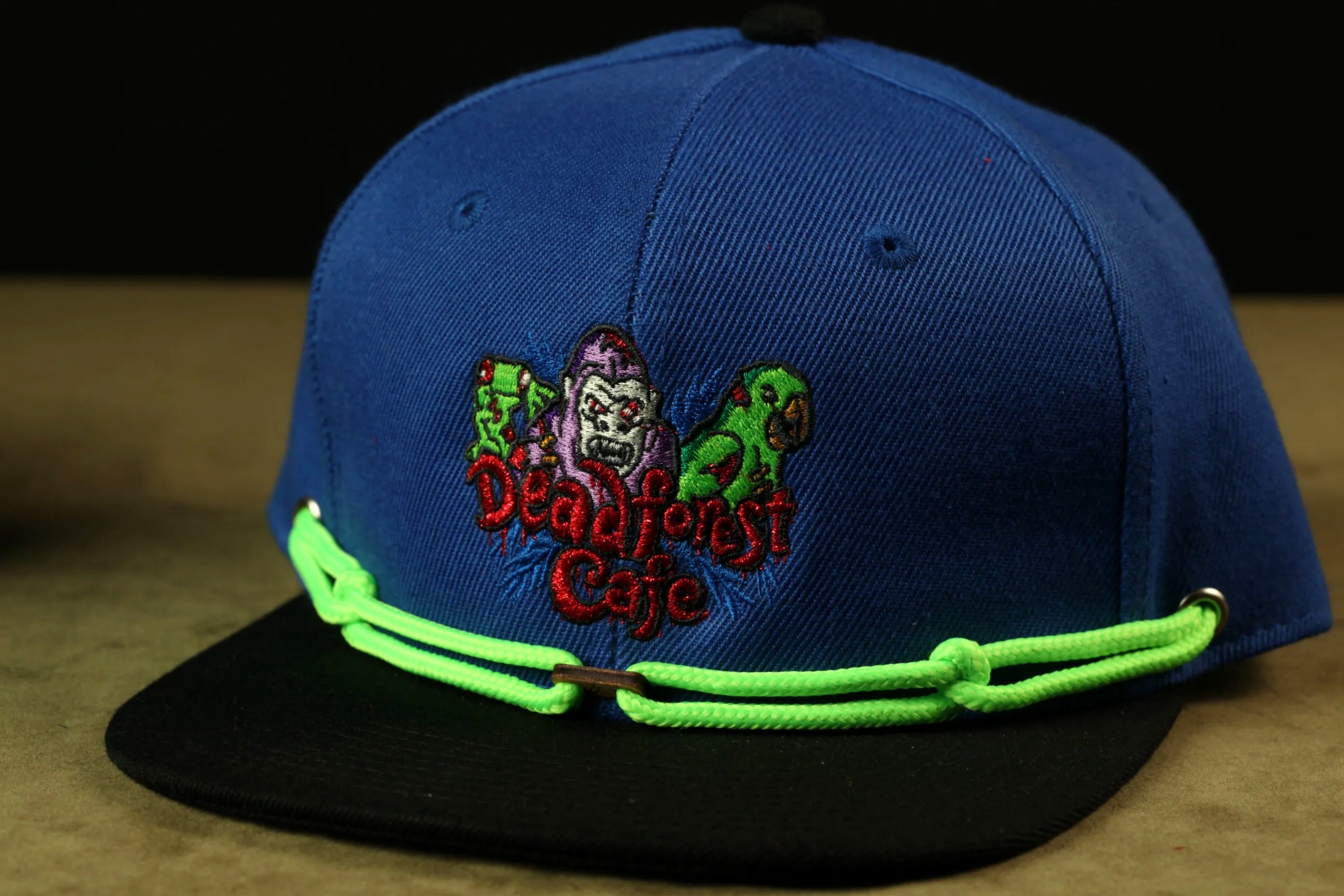 A blue baseball cap with a graphic design on it, featuring a character and the text "Deadliest Cafe".