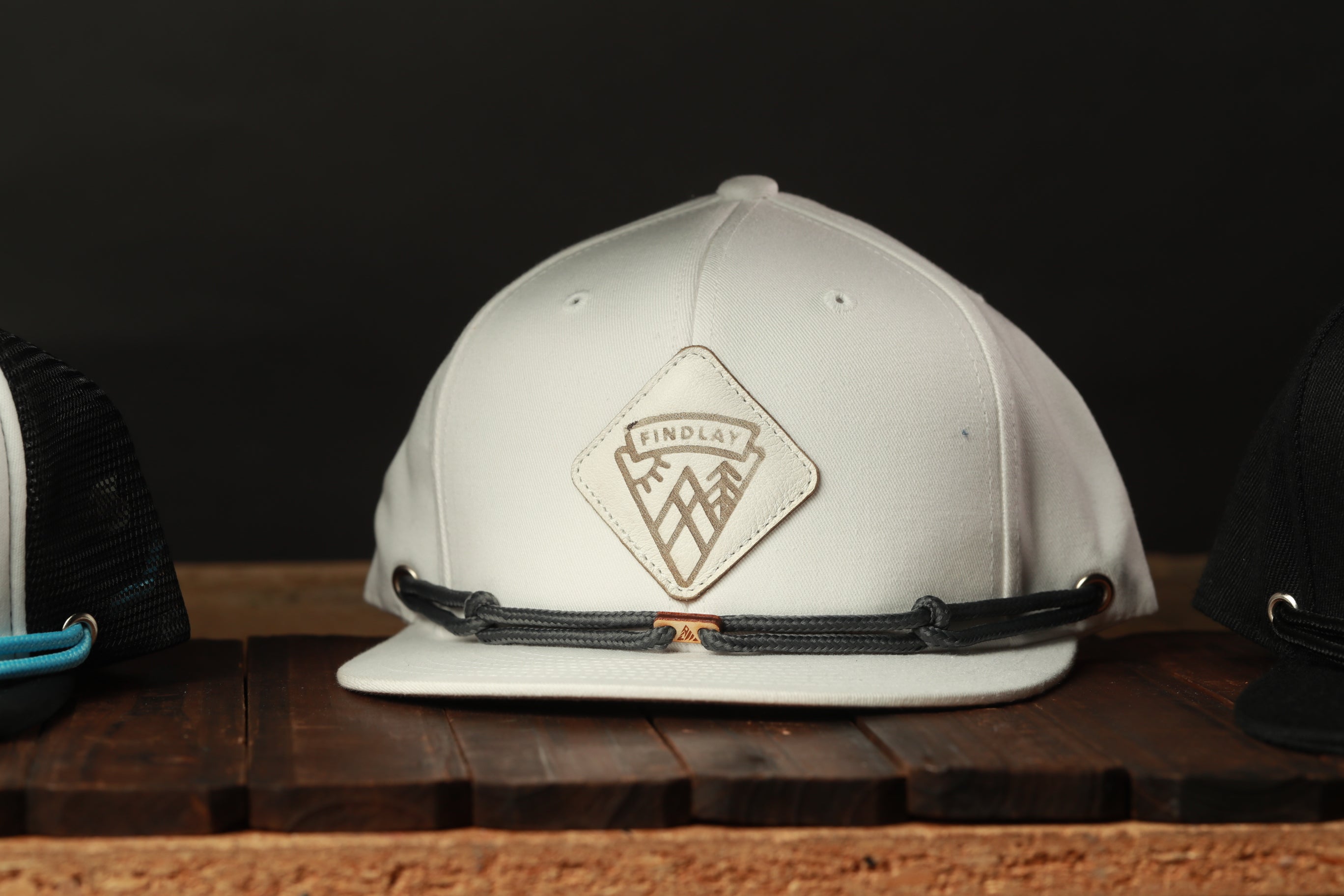 A white baseball cap with a logo on it, sitting on a wooden surface.