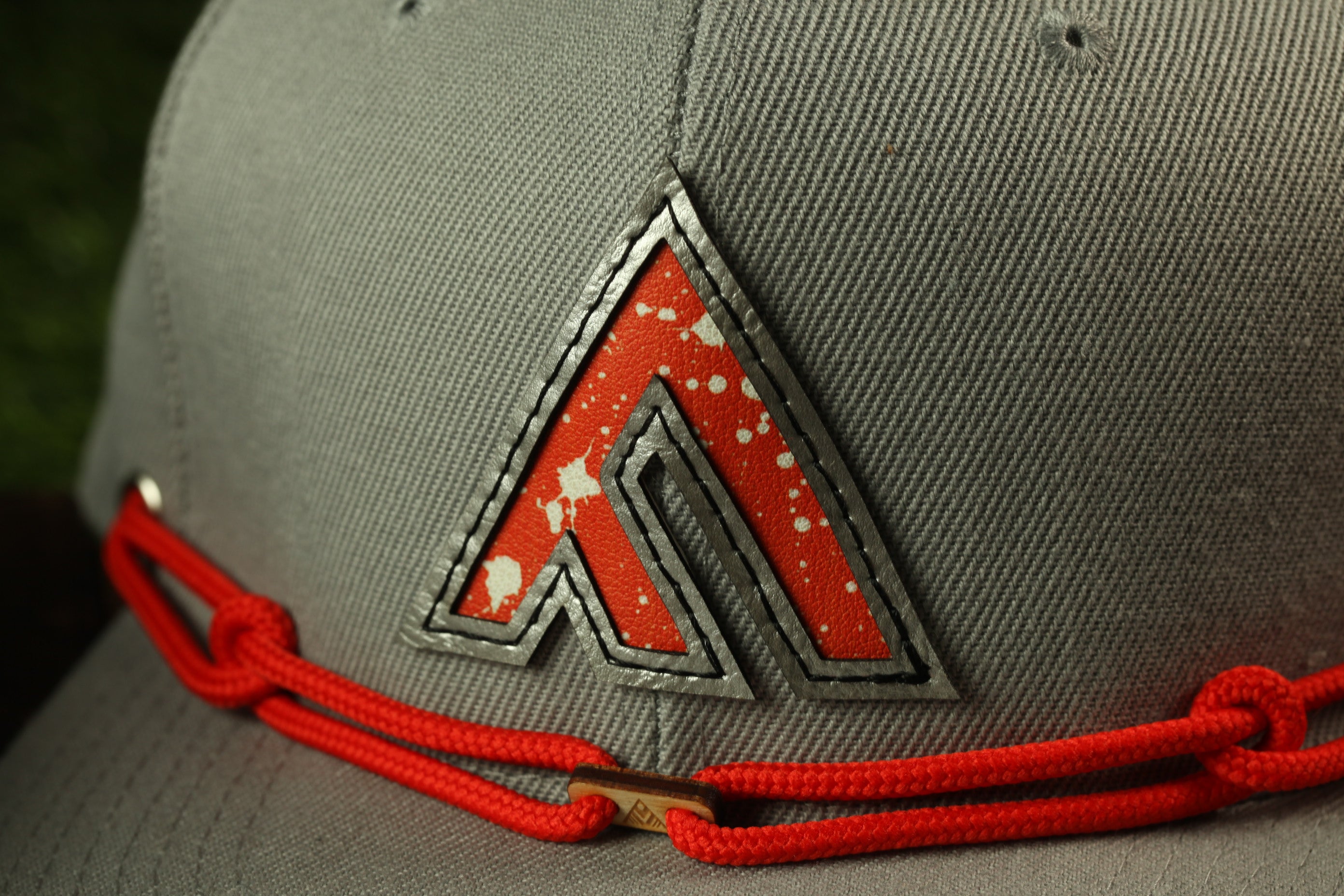 A close-up view of a gray baseball cap with a red and white logo on the front.