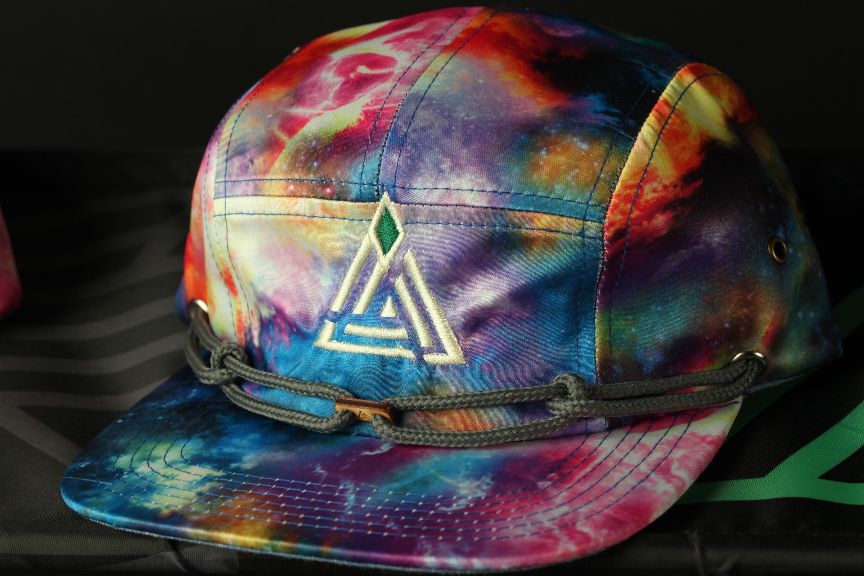 A colorful tie-dye baseball cap with a geometric pattern and a green logo on the front.