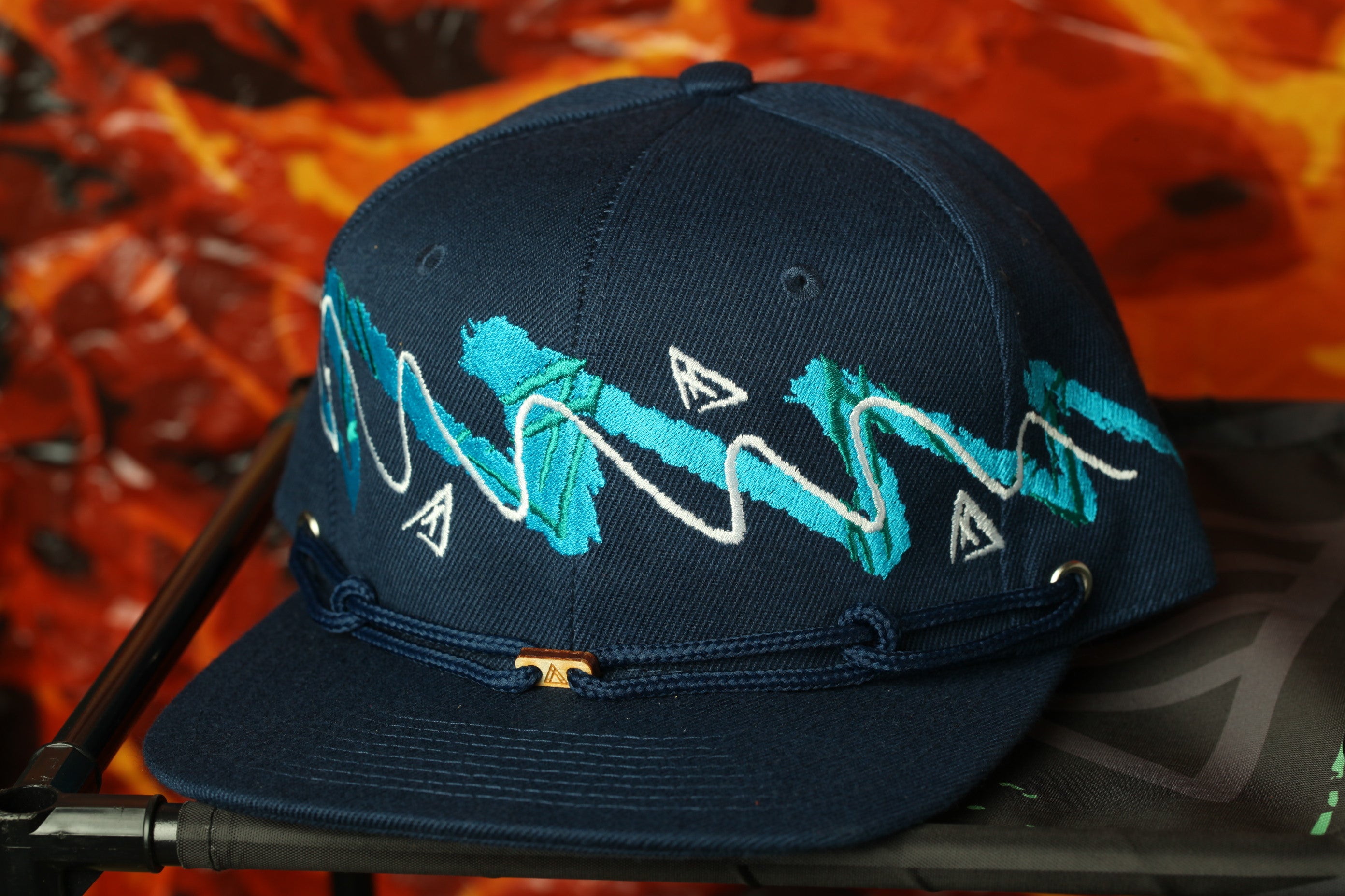 A navy blue baseball cap with a unique blue and white zigzag pattern on the front, sitting on a black surface against a vibrant orange background.