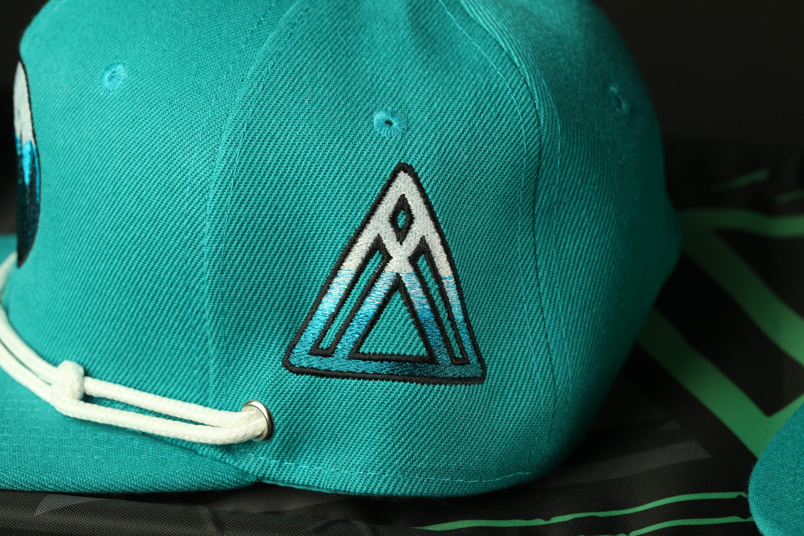 A close-up view of a teal-colored baseball cap with a white triangle logo on the side.