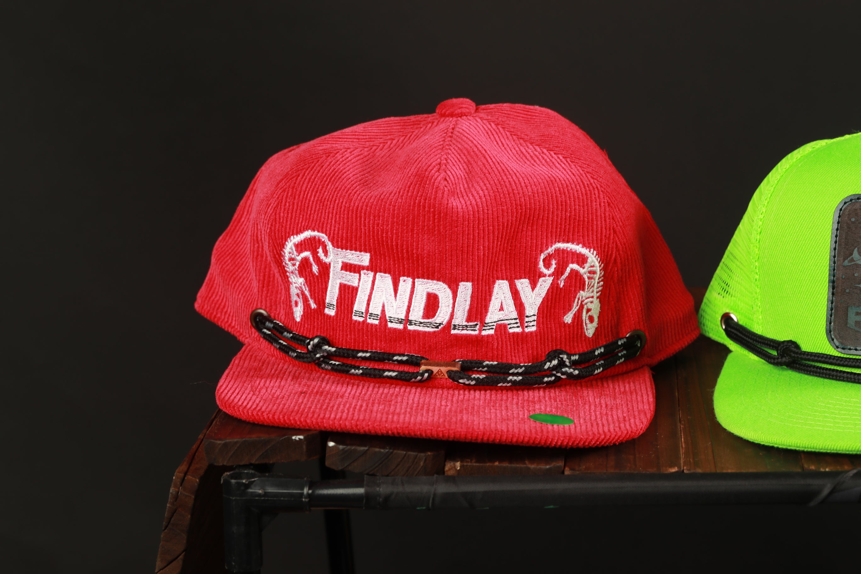 A red baseball cap with the word "FINDlay" printed on it, sitting on a wooden surface.