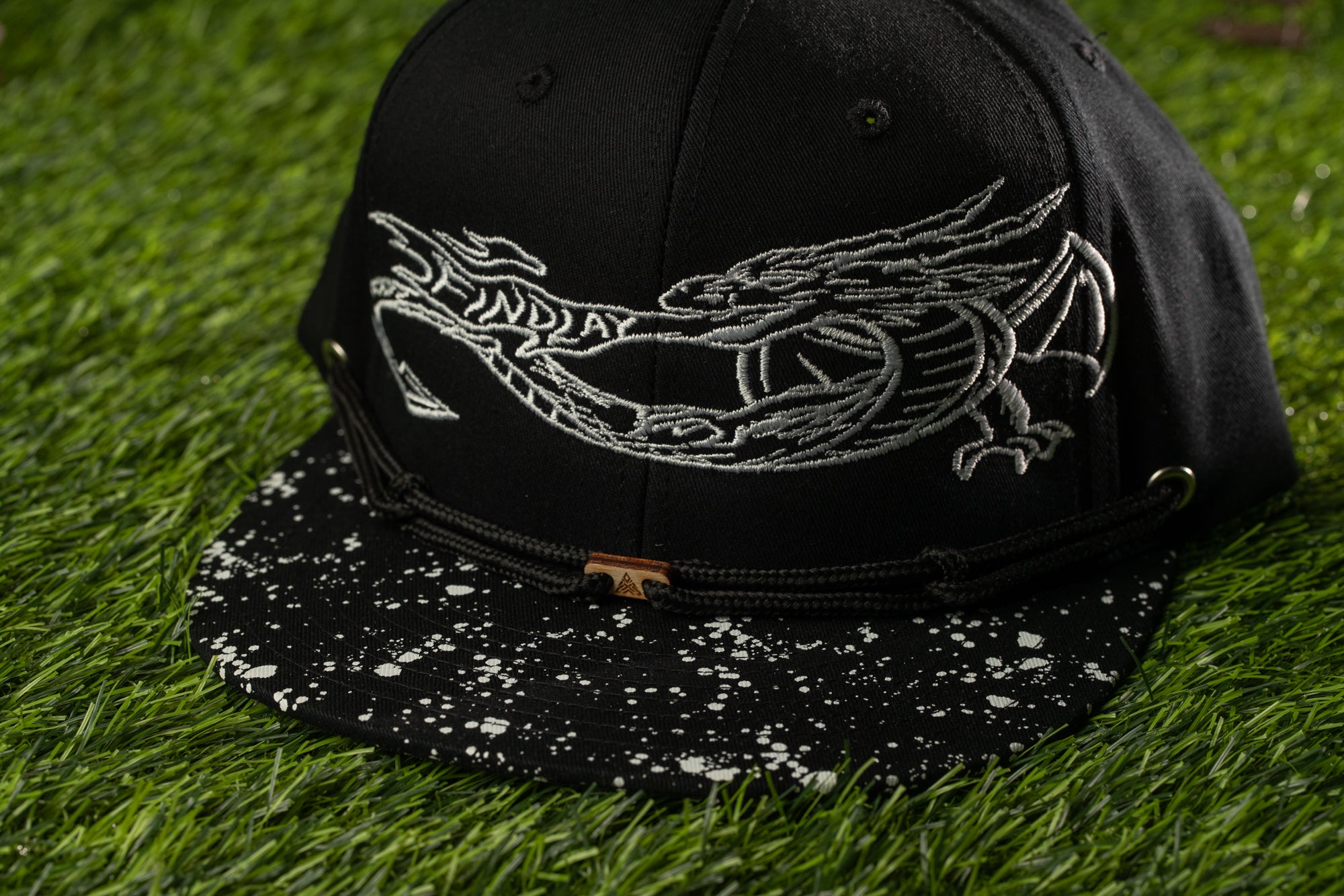 A black baseball cap with a white dragon design on it, placed on a grassy surface.