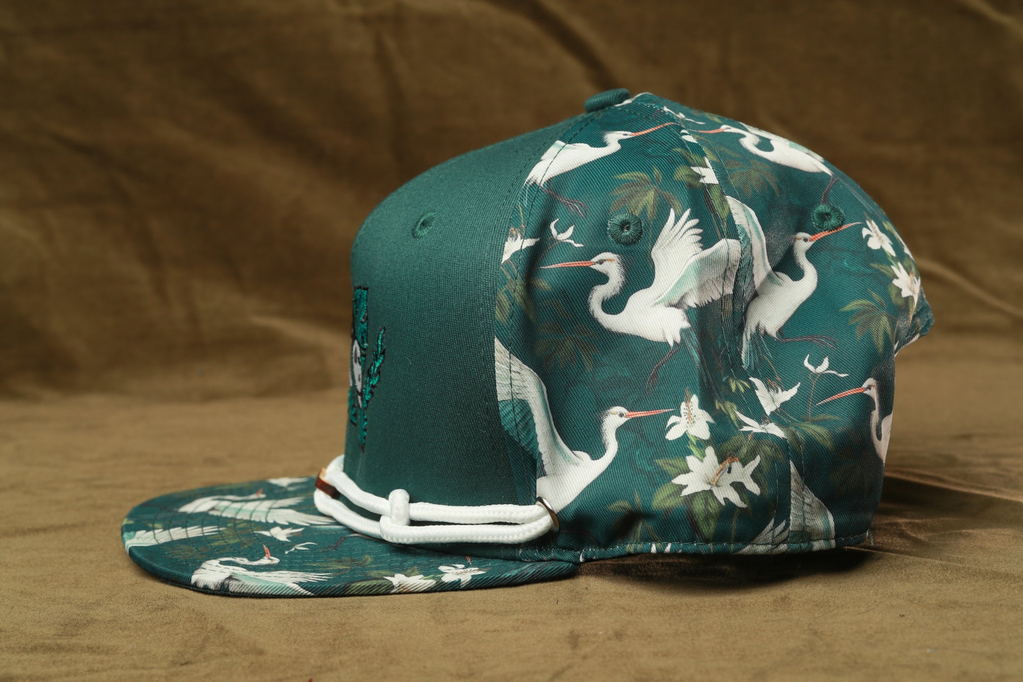 A green baseball cap with a floral pattern on the front and back, featuring white birds and flowers.