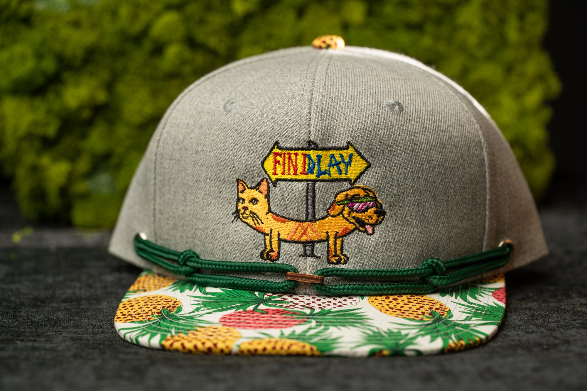 A gray baseball cap with a colorful embroidered design on the front, featuring a cat and a sign that says "Findlay".
