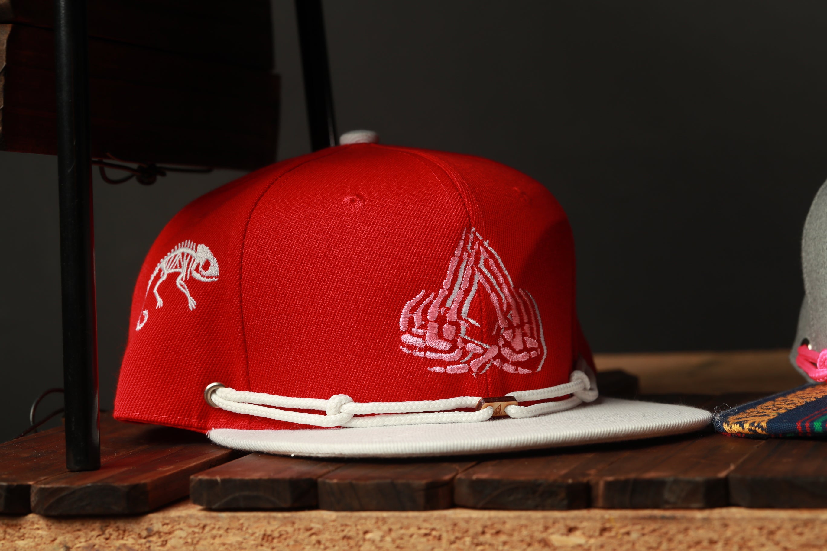 A red baseball cap with a white strap and a white graphic design on the front, placed on a wooden surface.