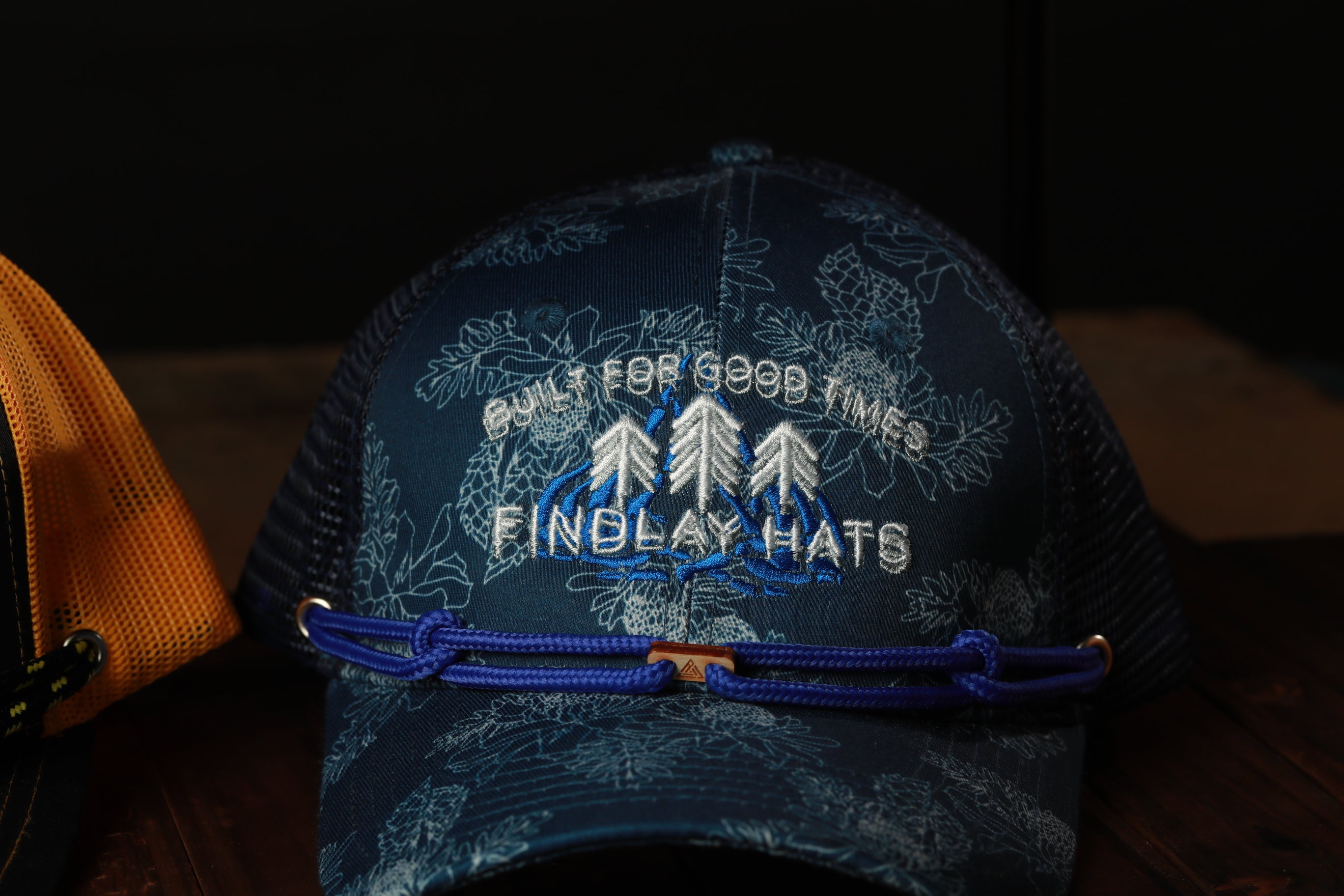 A blue baseball cap with a floral pattern and the text "BUILT FOR GOOD TIMES FINDLAY HATS" printed on it.