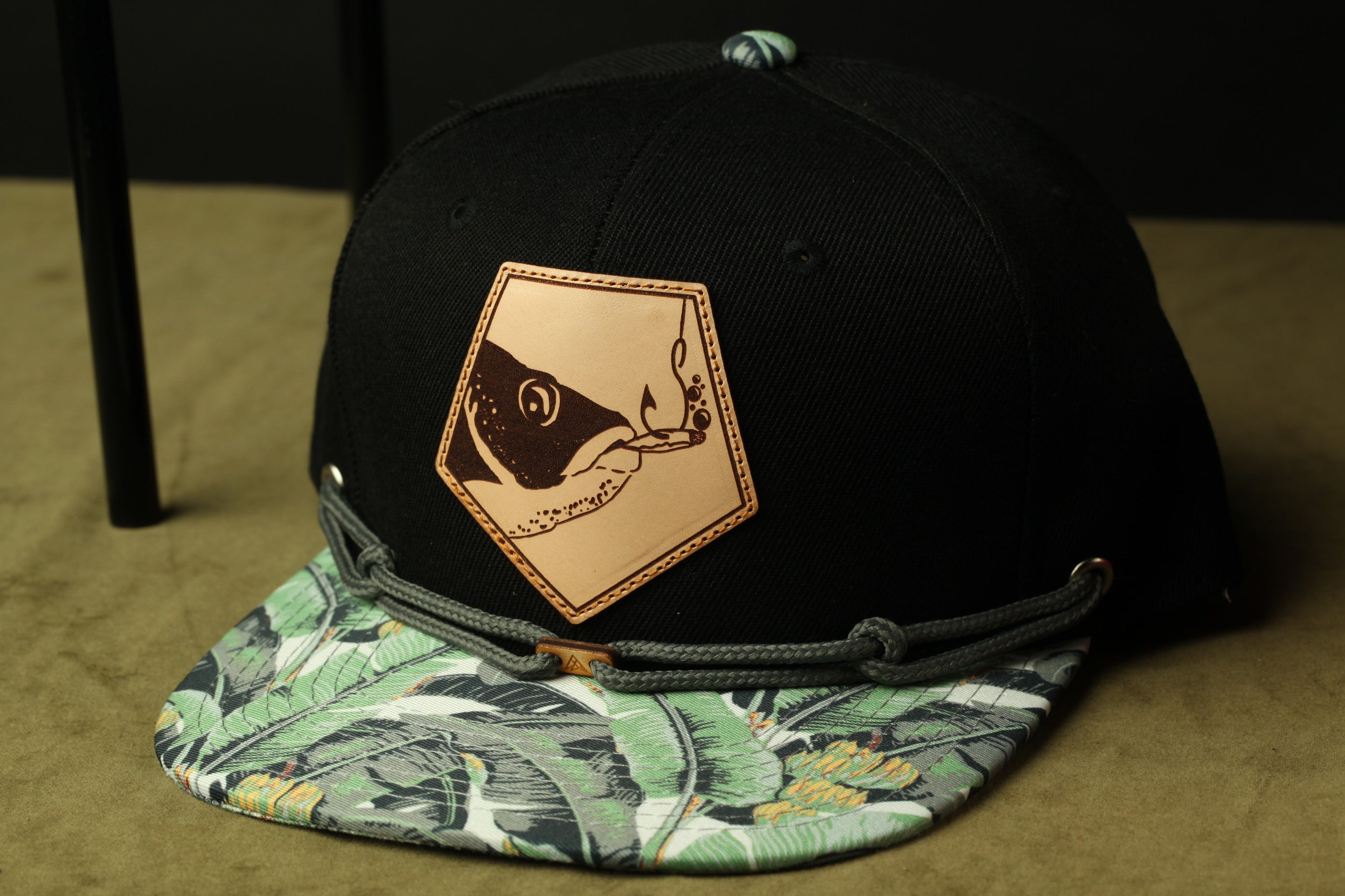 A black baseball cap with a printed pattern and a patch featuring a fish design.