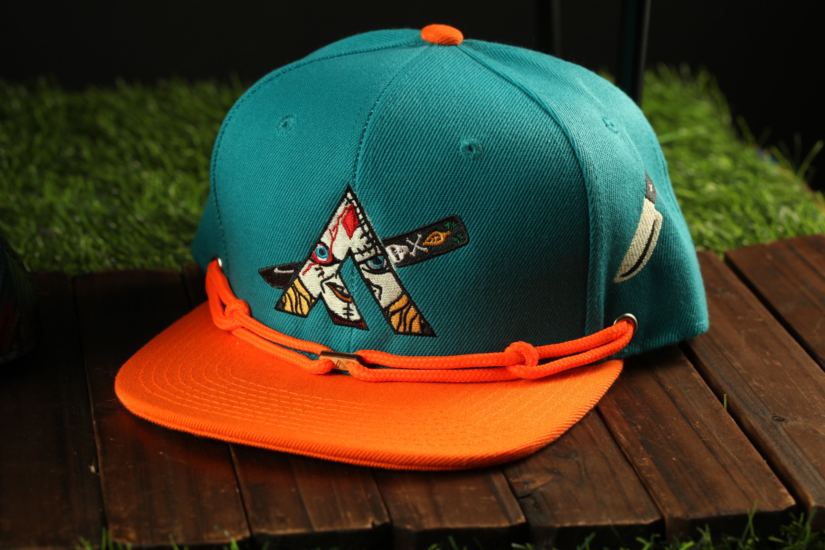 A turquoise baseball cap with an orange brim and a graphic design on the front, placed on a wooden surface.