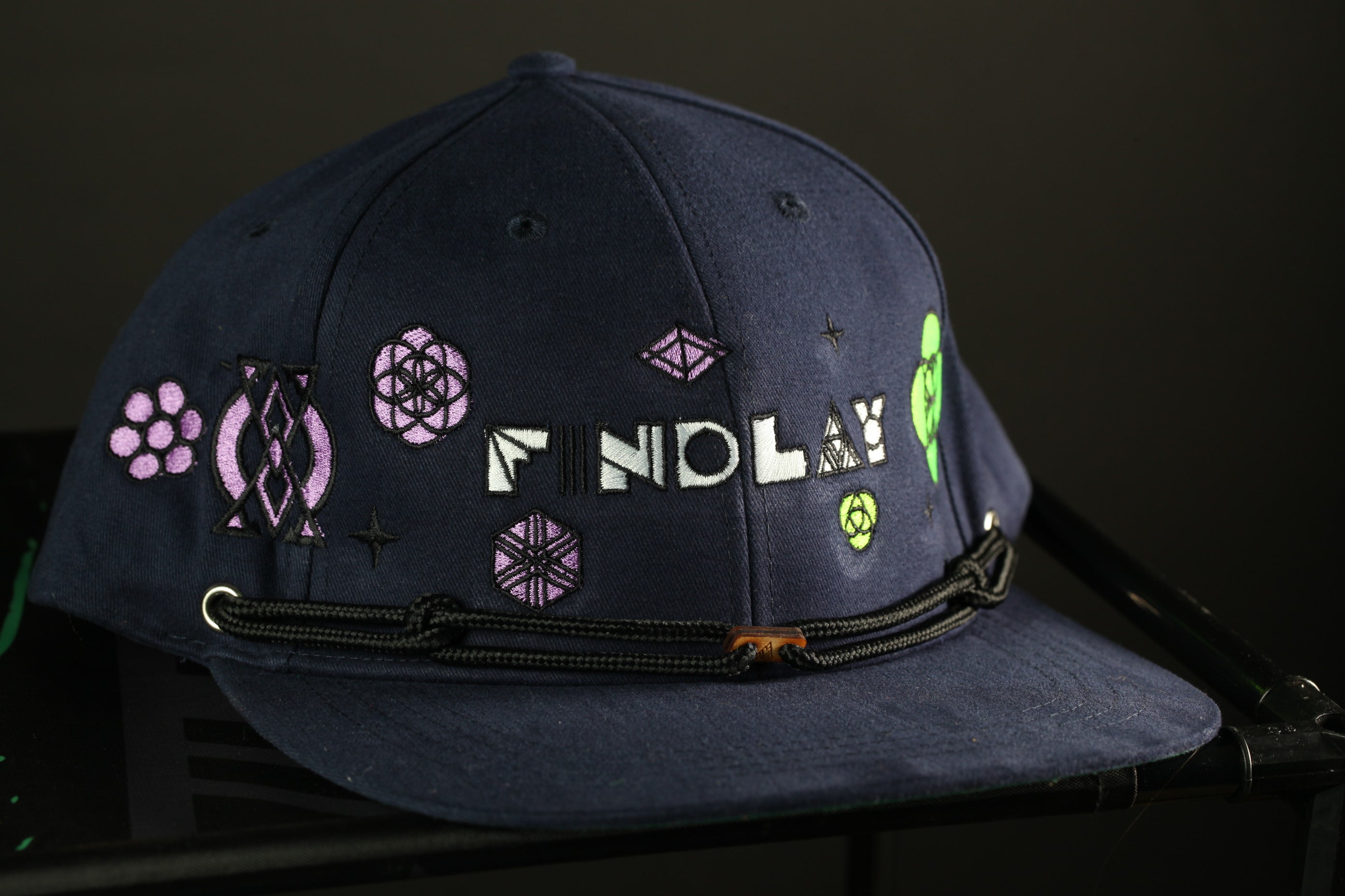 A navy blue baseball cap with various colorful designs and text on it.