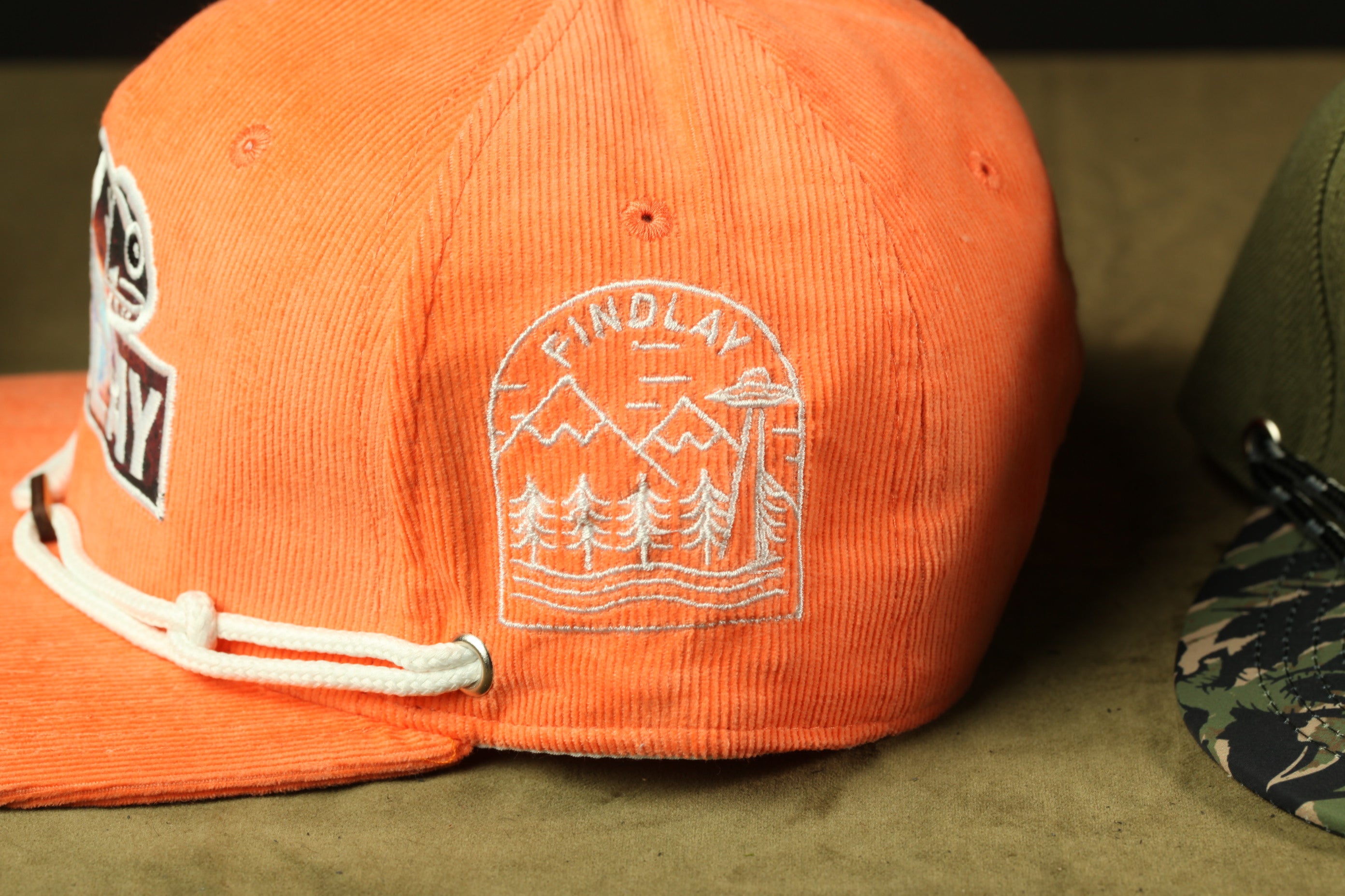a close-up view of an orange baseball cap with a white embroidered design on the side.