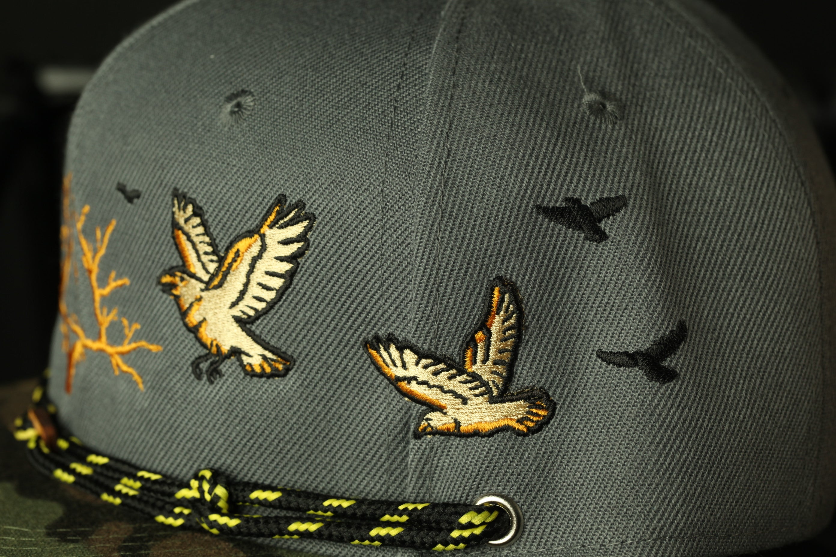 A close-up view of a gray baseball cap with embroidered images of birds in flight.