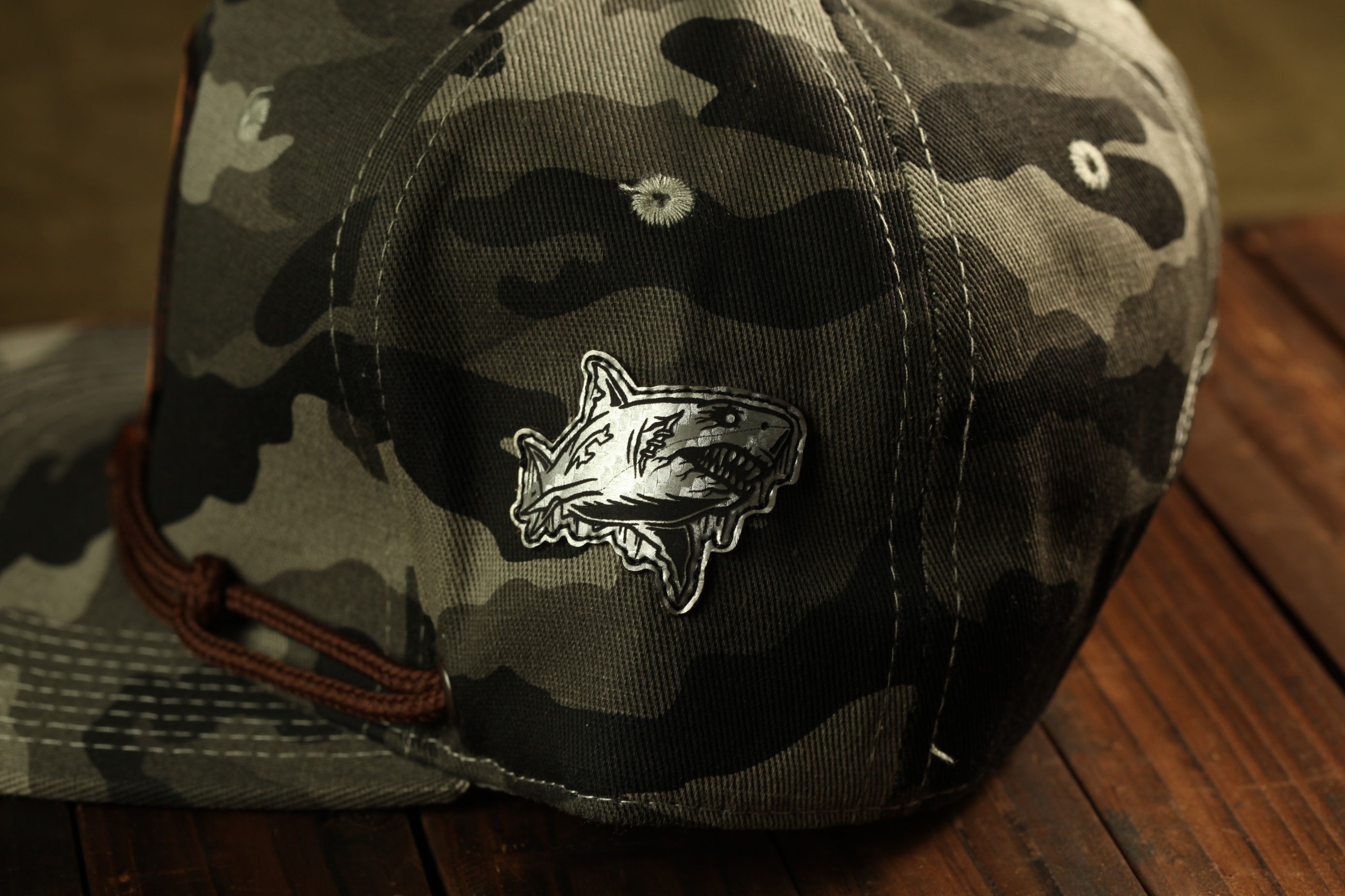 A camouflage baseball cap with a shark patch on the front.