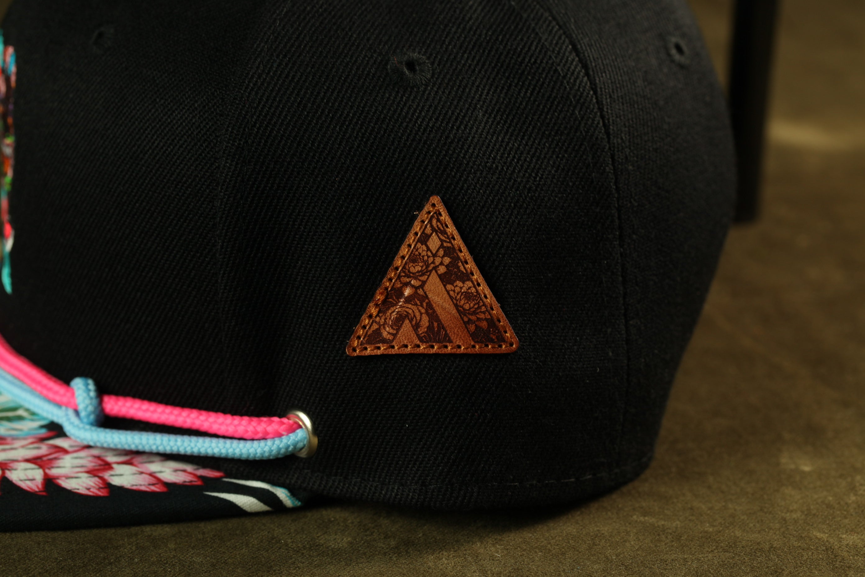 A close-up view of a black baseball cap with a leather patch on the front, featuring a floral design.