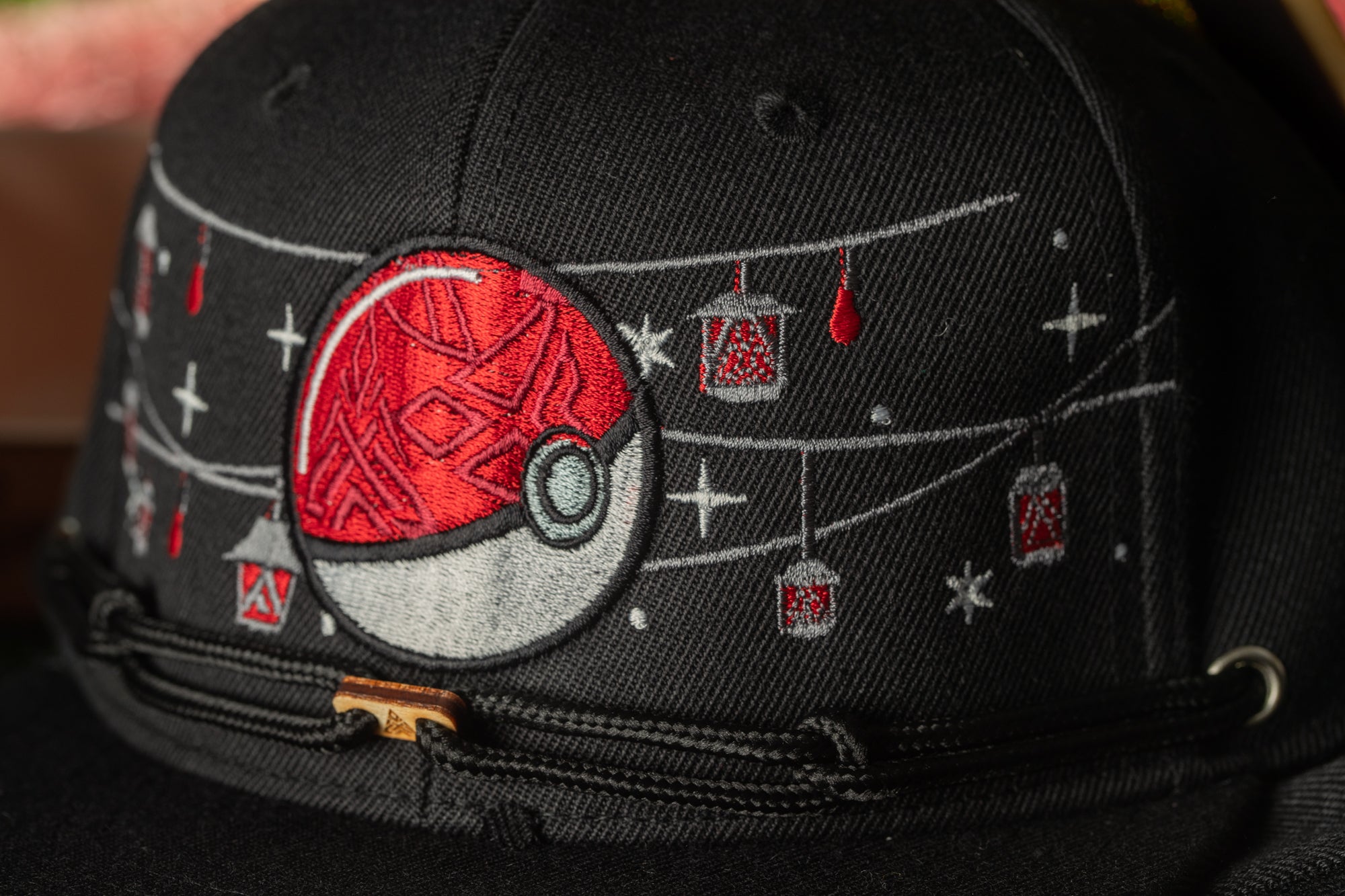 A close-up view of a black baseball cap with a red and white Pokemon-inspired design on the front.