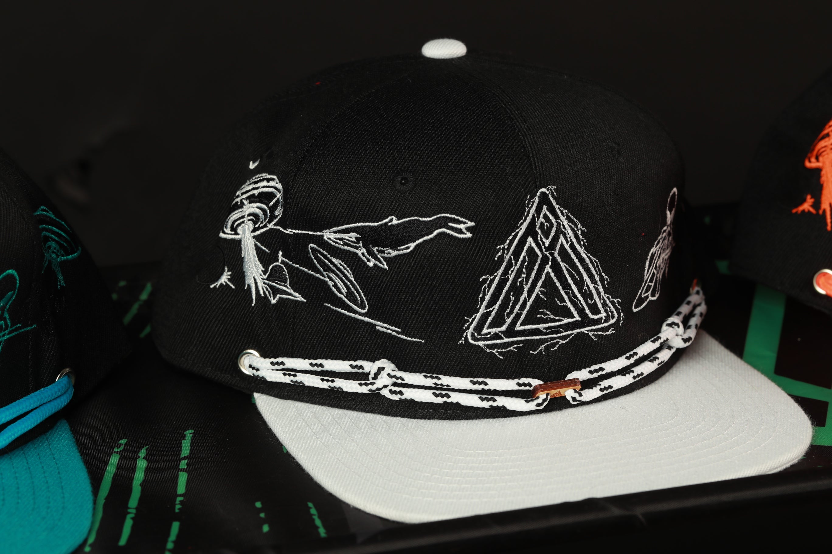 A black baseball cap with white embroidered designs on it, including a triangle and a bird.