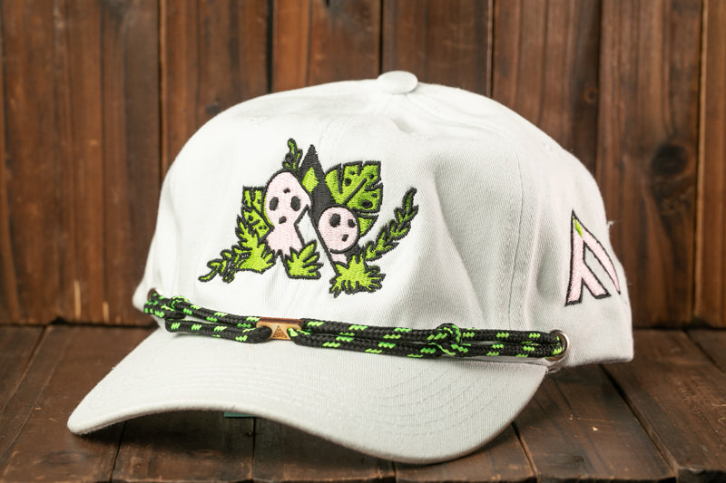 A white baseball cap with a green and black braided strap, featuring an embroidered design of two ghostly figures on the front.
