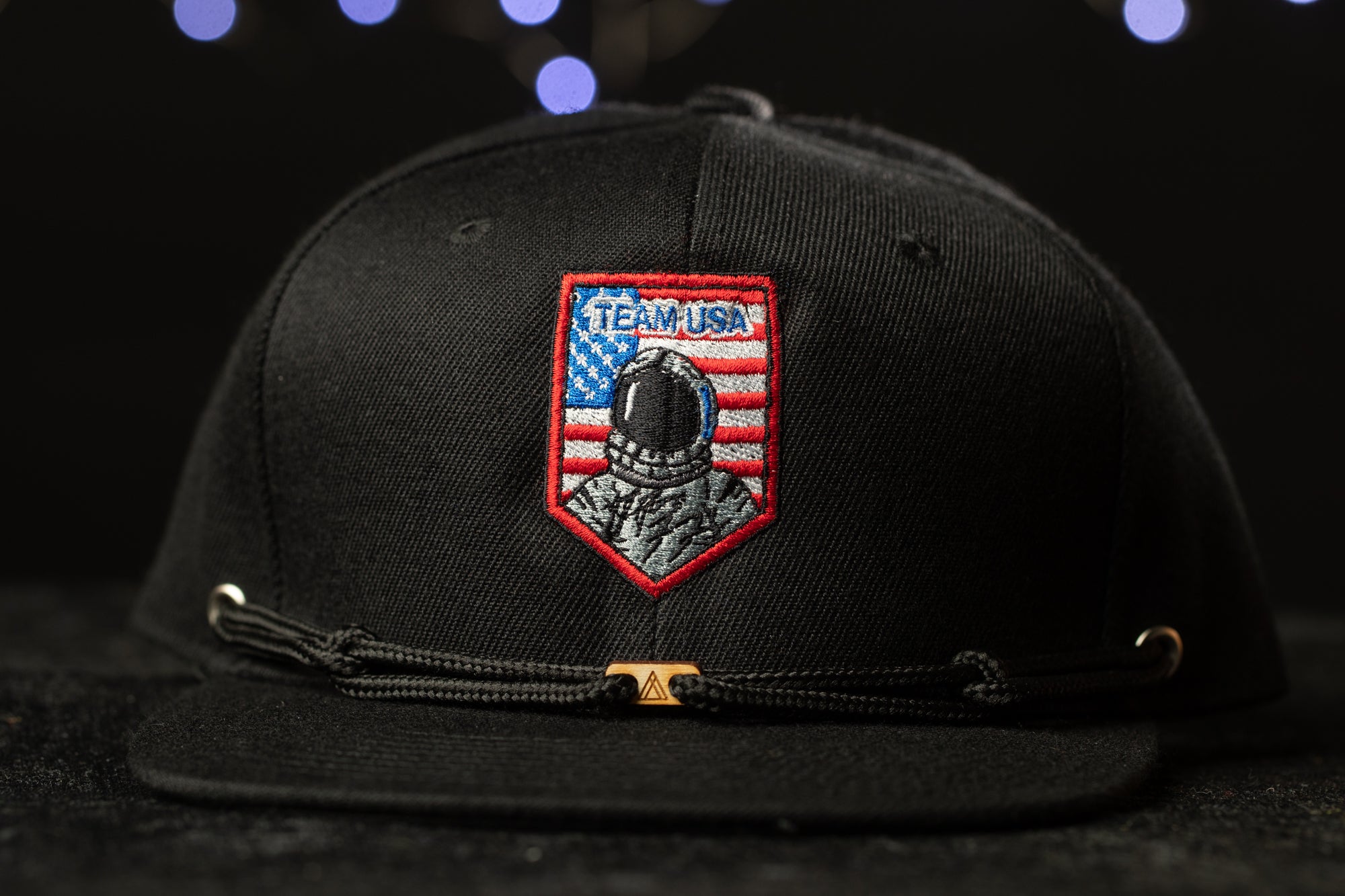 A black baseball cap with a red and blue patch on the front, featuring an astronaut and the text "TEAM USA".