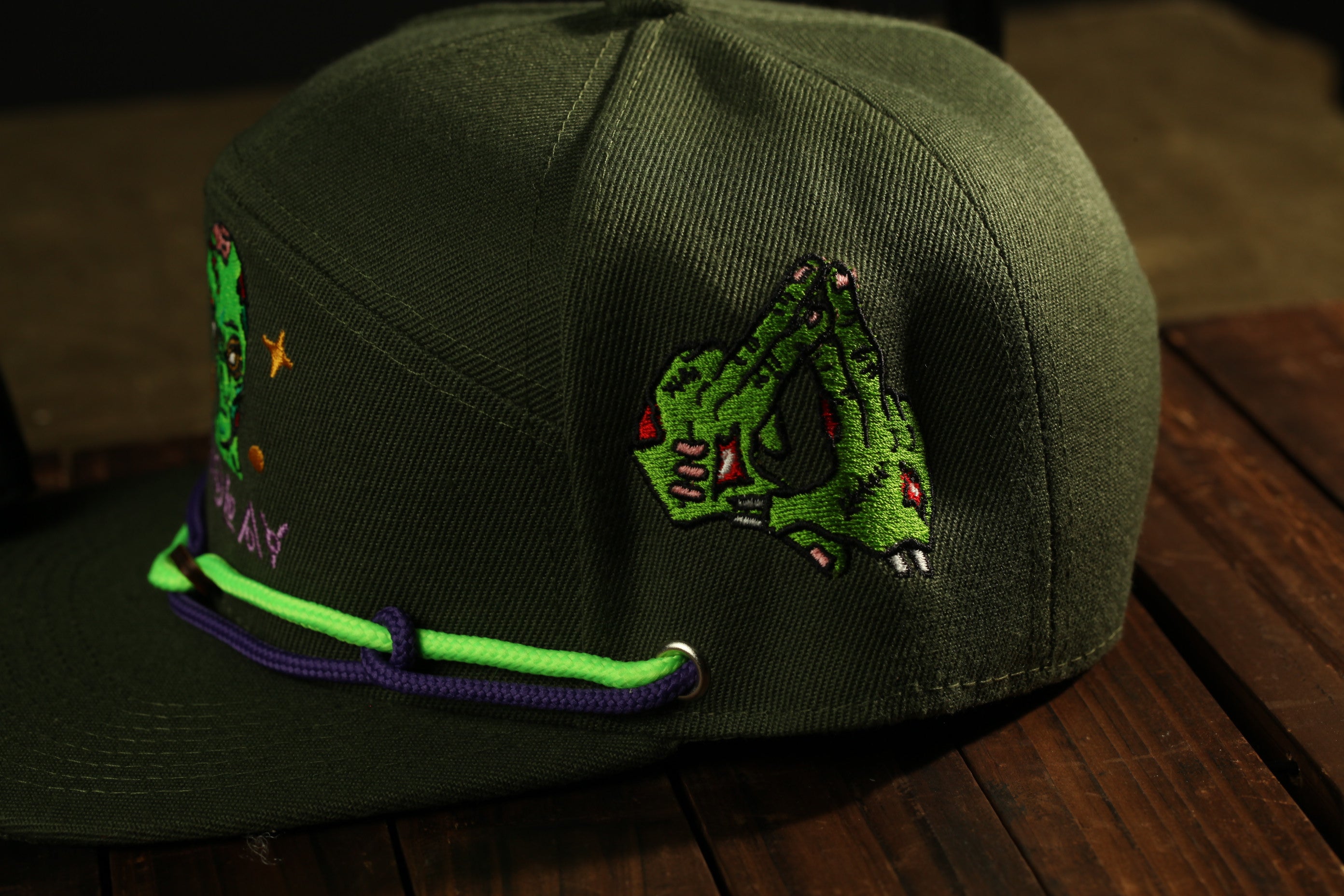 A close-up view of a dark green baseball cap with a unique embroidered design on the side.