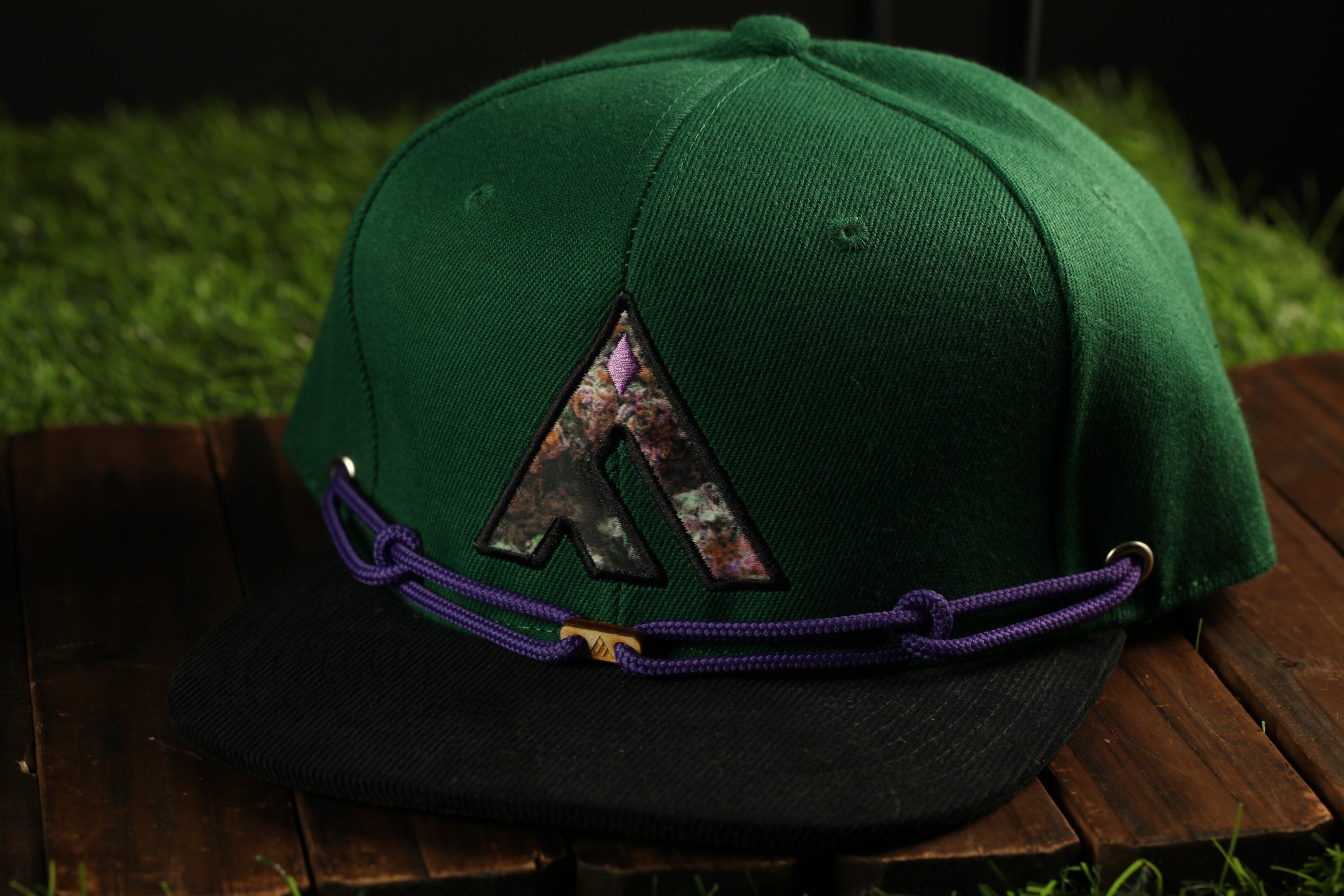 A green baseball cap with a purple and black logo on it, placed on a wooden surface.