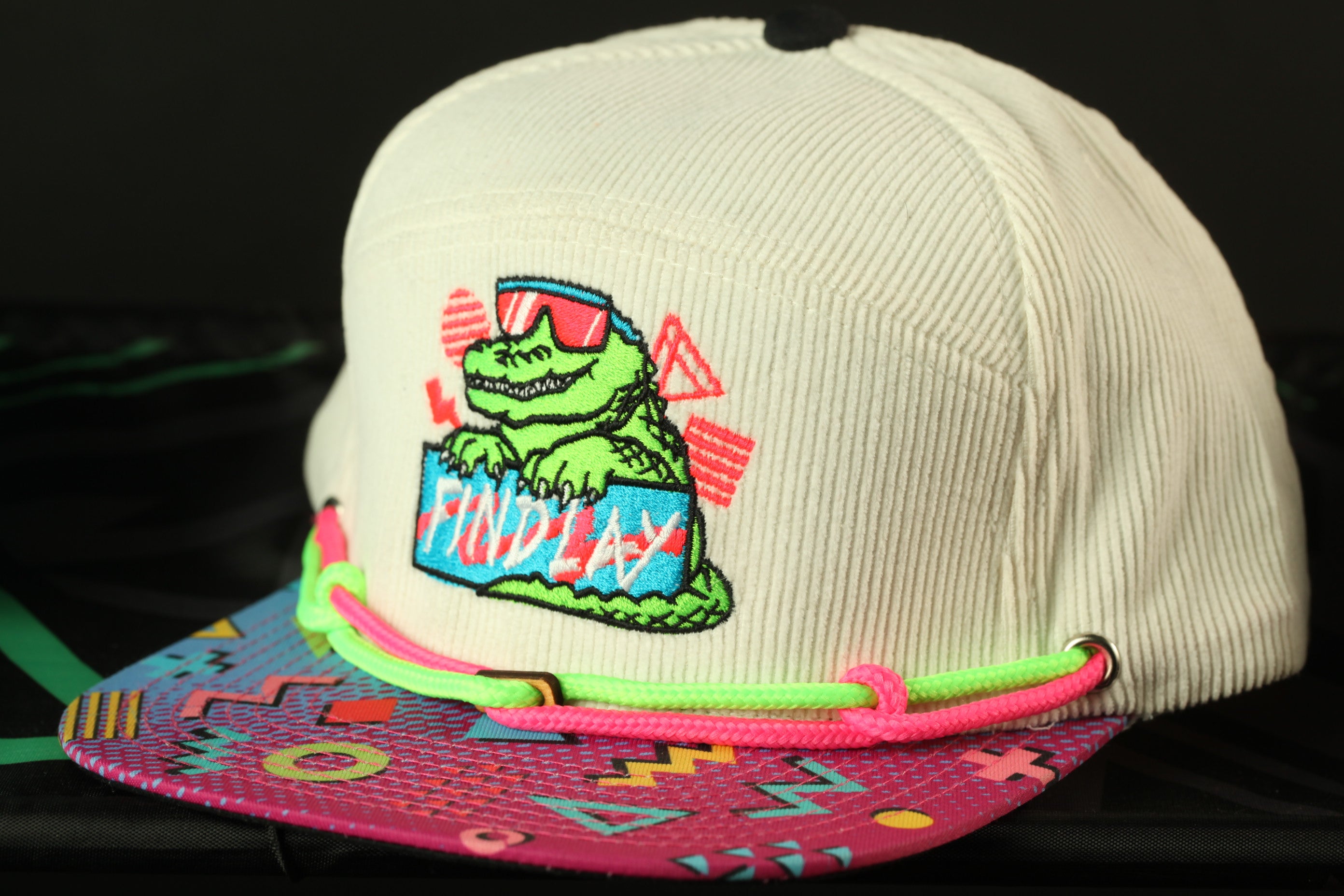 A white baseball cap with a colorful graphic and text on it, placed on a surface with a patterned design.