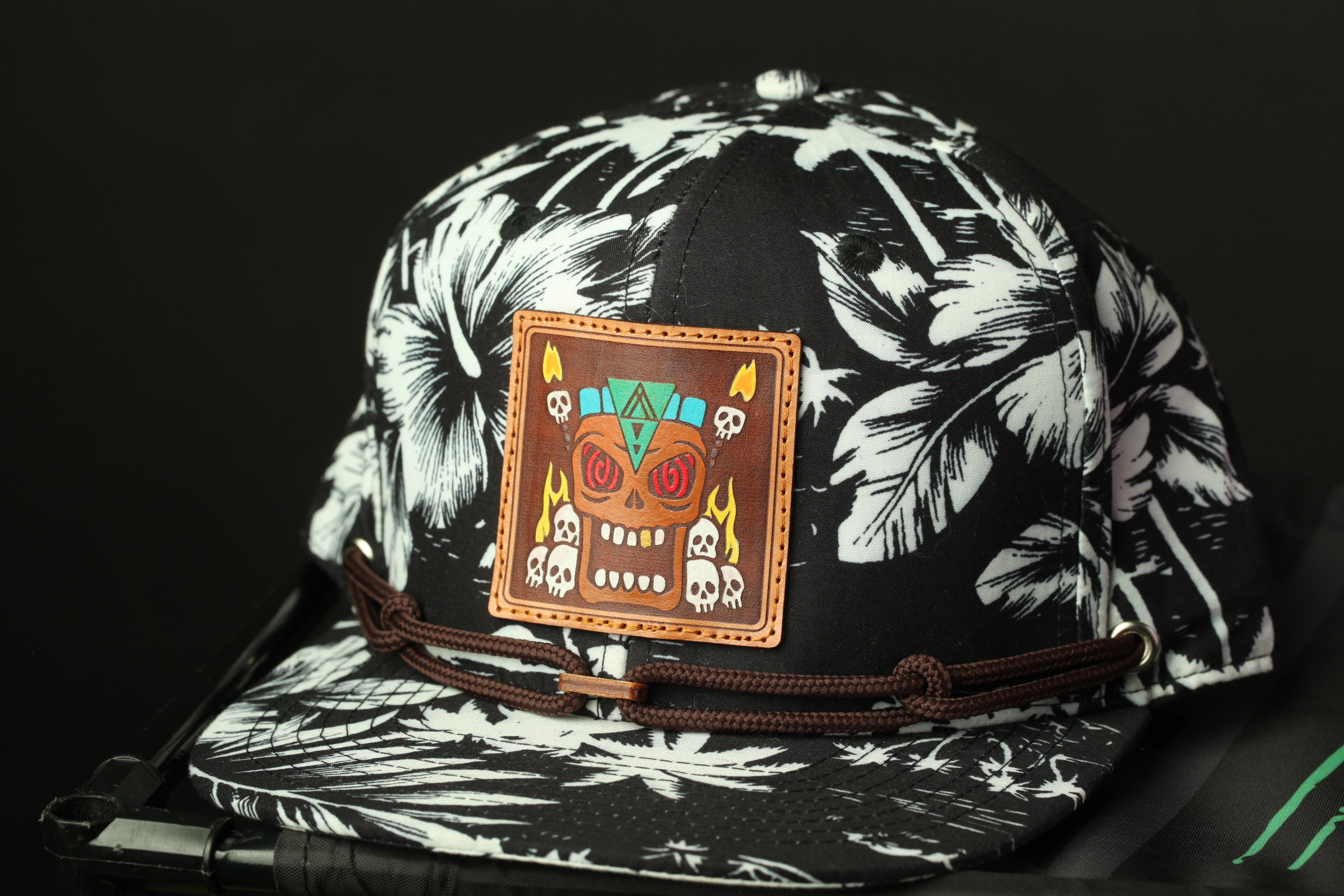 A black and white tropical-themed baseball cap with a colorful skull and floral design on the front.