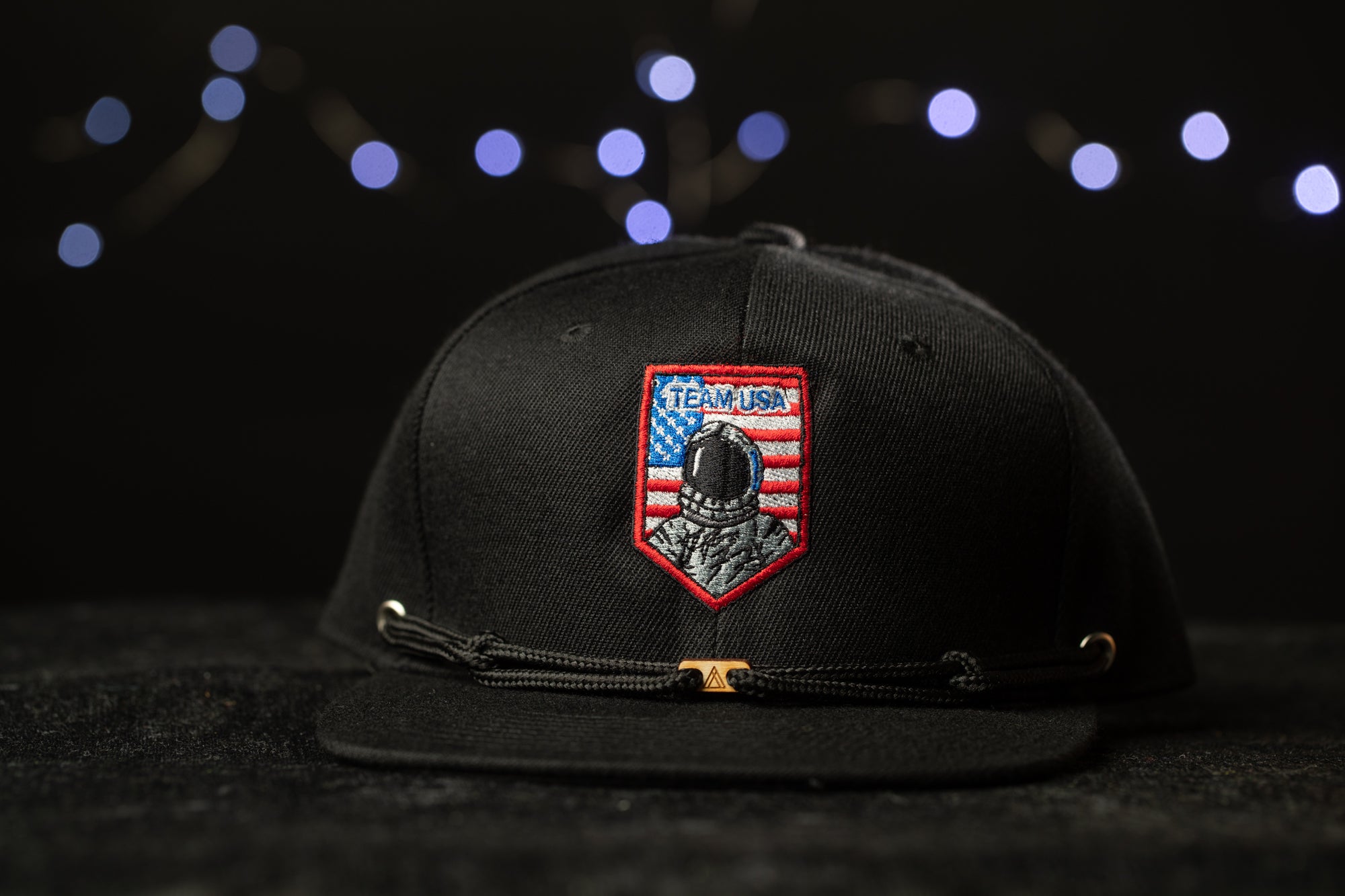 A black baseball cap with a red and blue patch on the front, featuring an image of a person wearing a helmet and the text "TEAM USA" on the patch.