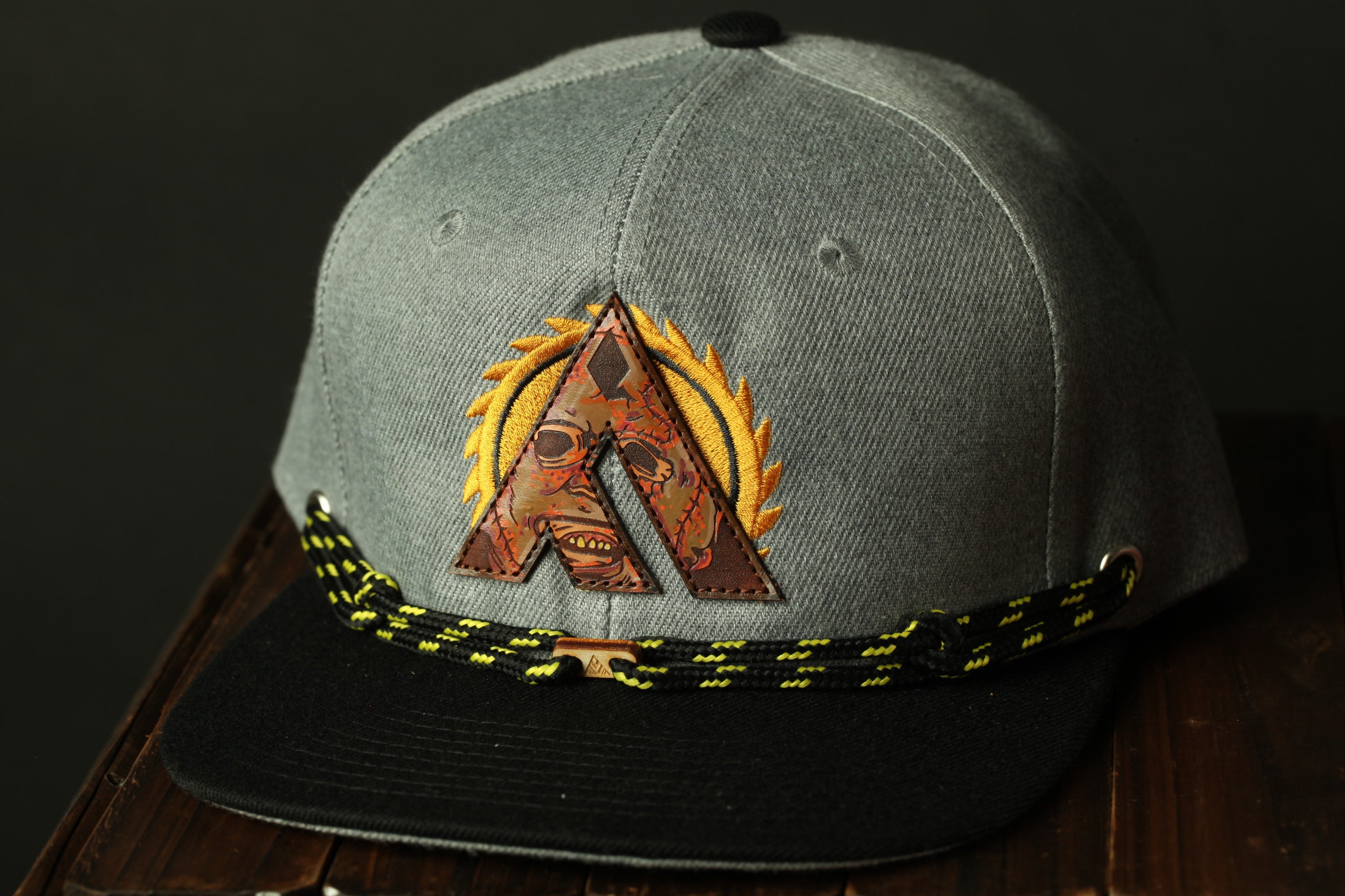 A gray baseball cap with a black brim and a black and yellow braided strap.