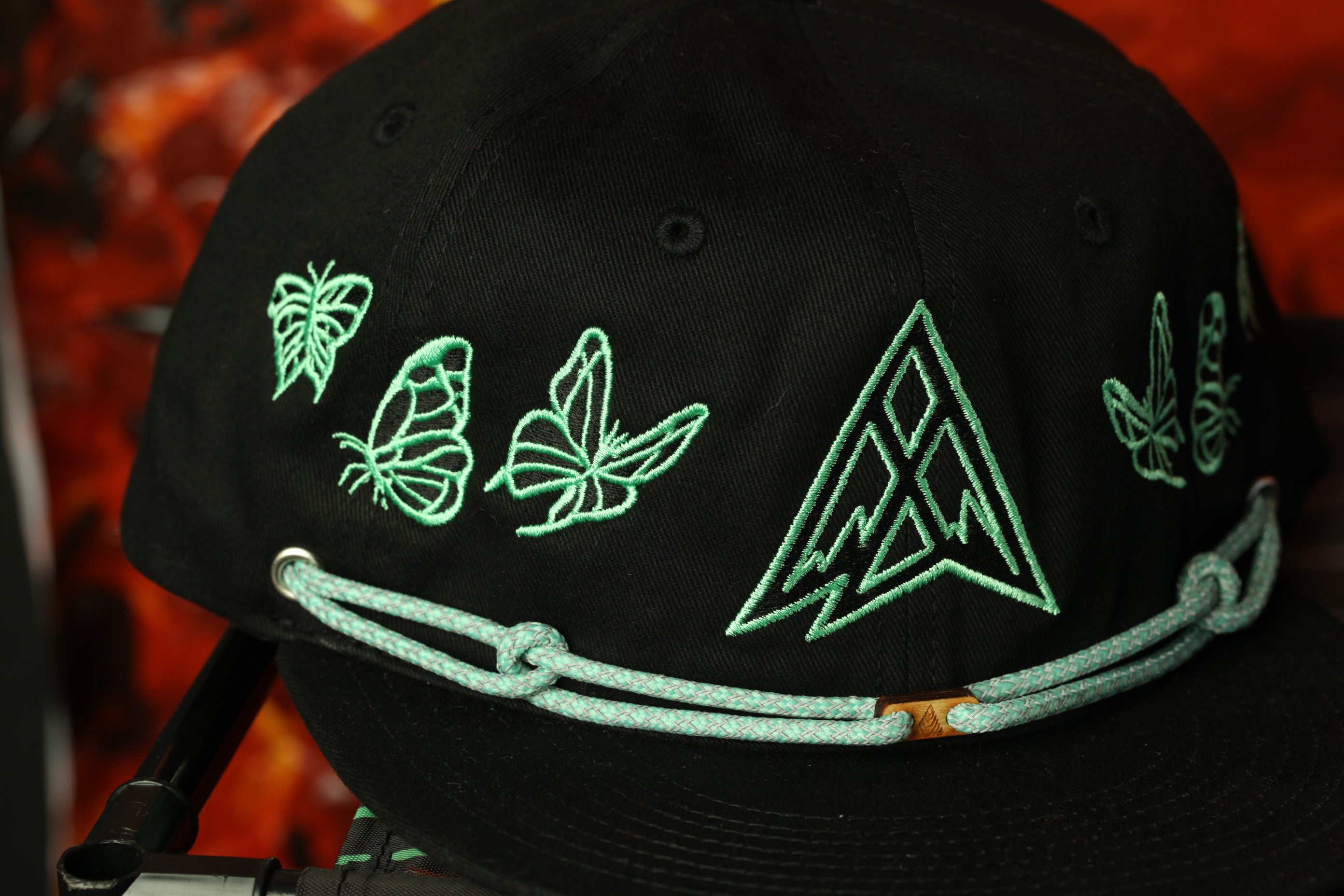 A black baseball cap with green embroidered butterflies and a triangle design on the front.