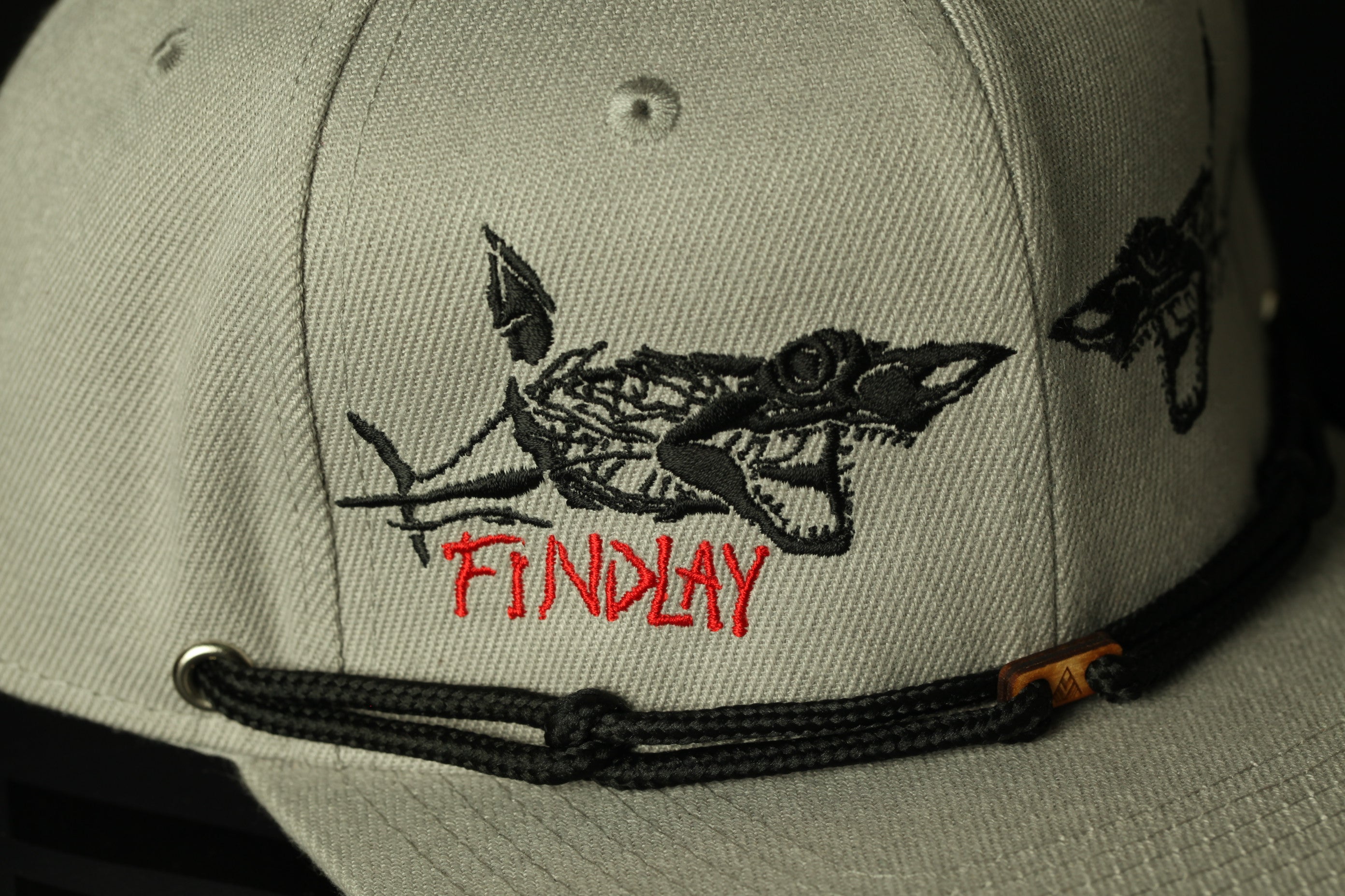 A close-up of a gray baseball cap with a black shark embroidered on it, and the word "FINDlay" printed in red on the front.