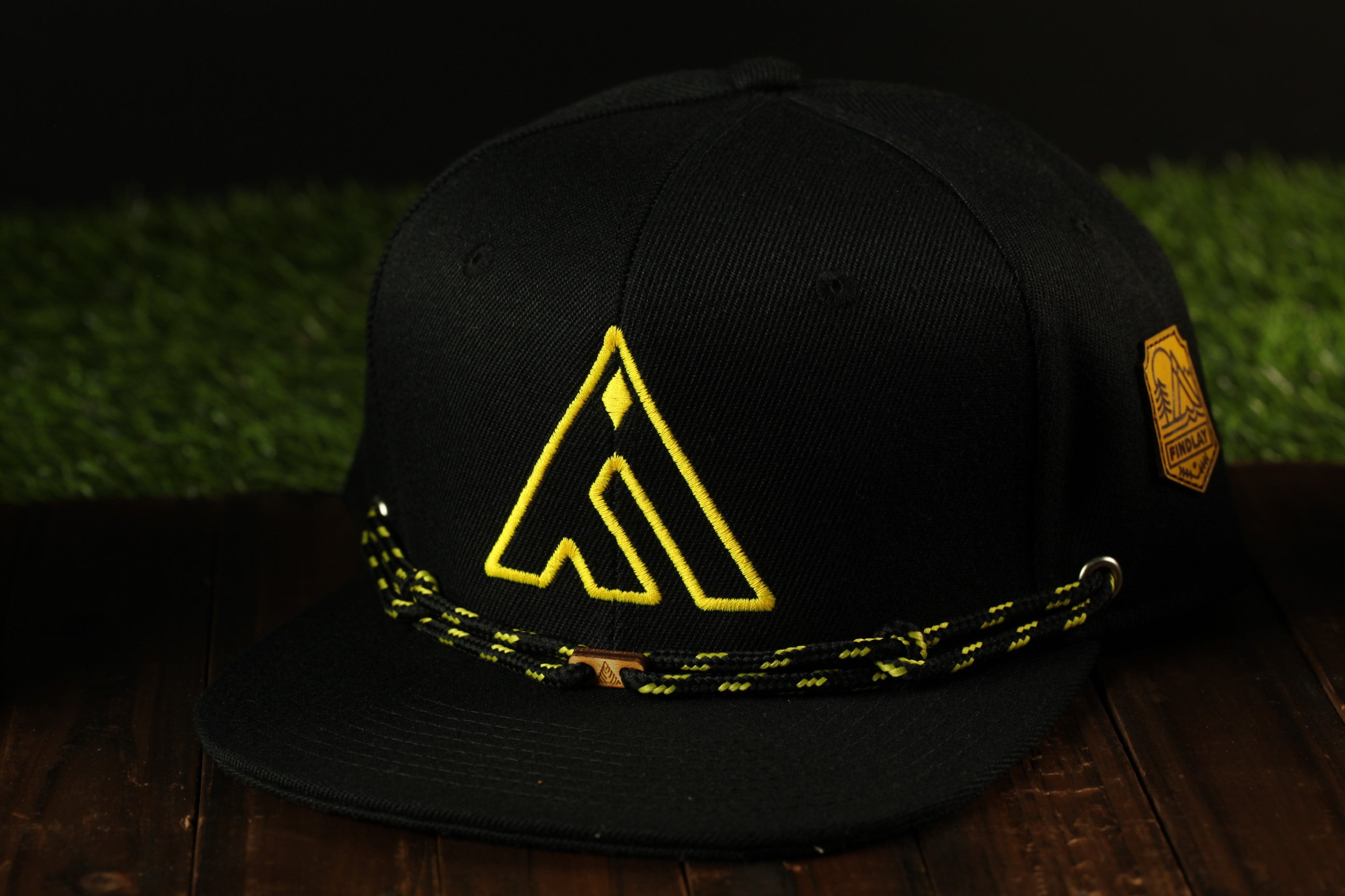 A black baseball cap with a yellow logo on it, placed on a wooden surface.