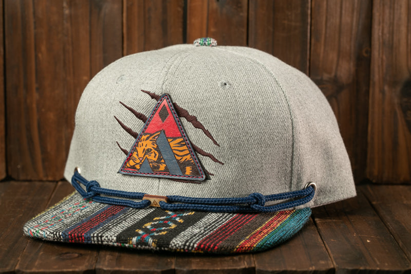 A gray baseball cap with a colorful, patterned brim and a patch featuring a tiger design, placed on a wooden surface.