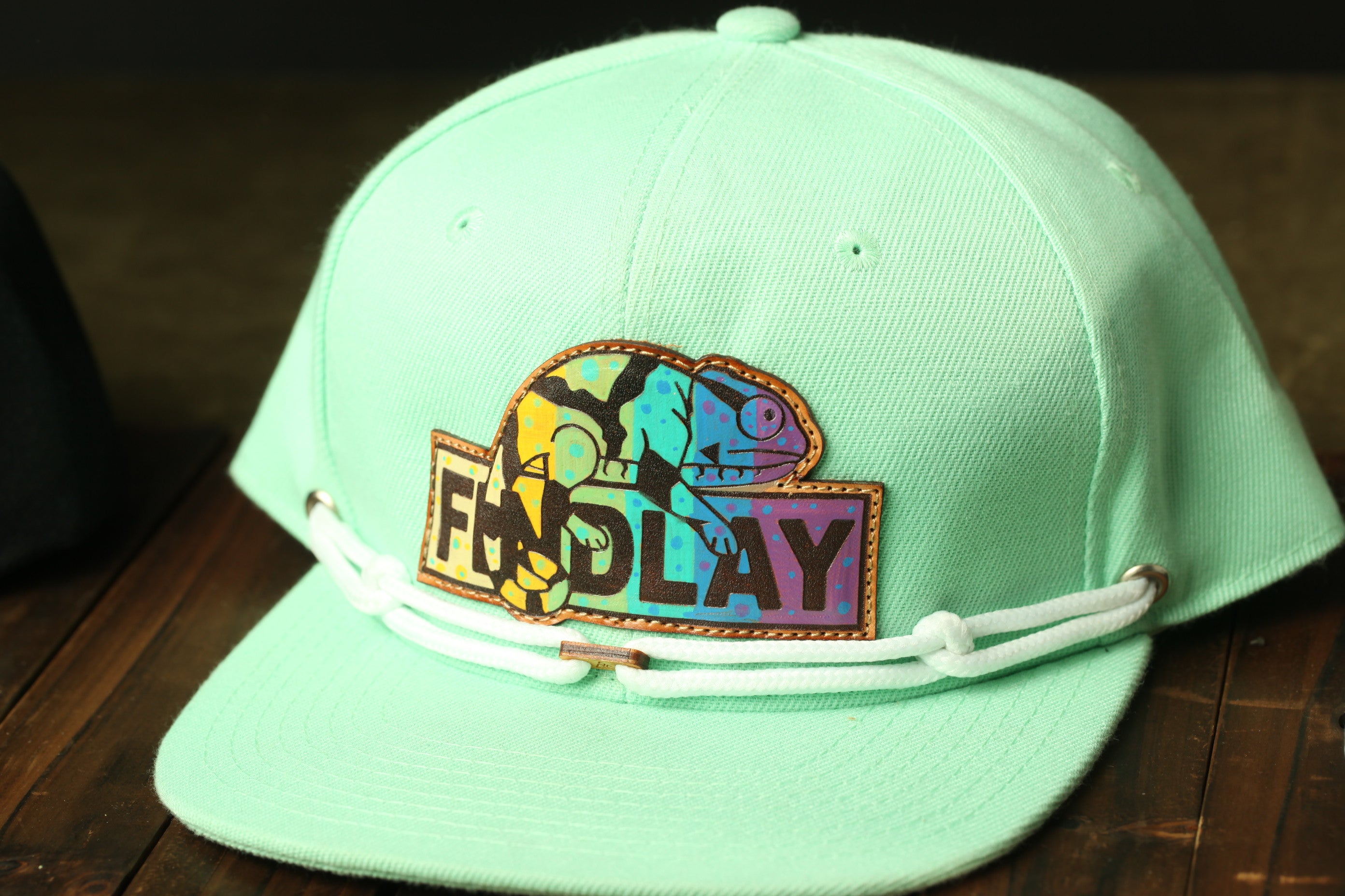 A mint green baseball cap with a colorful patch featuring a chameleon and the word "FENDLAY" printed on it.