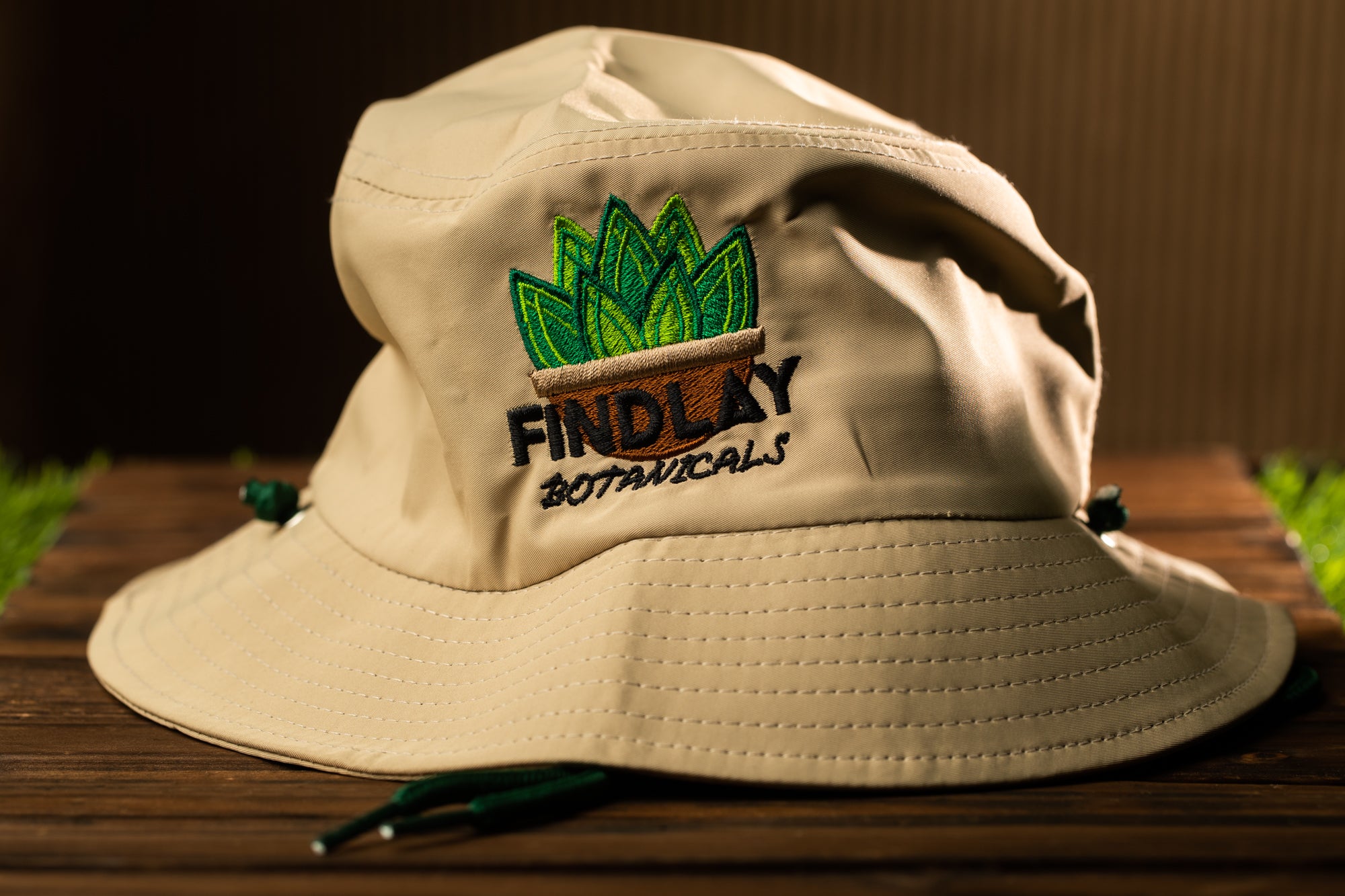 A beige bucket hat with a green plant embroidered on it, sitting on a wooden surface.