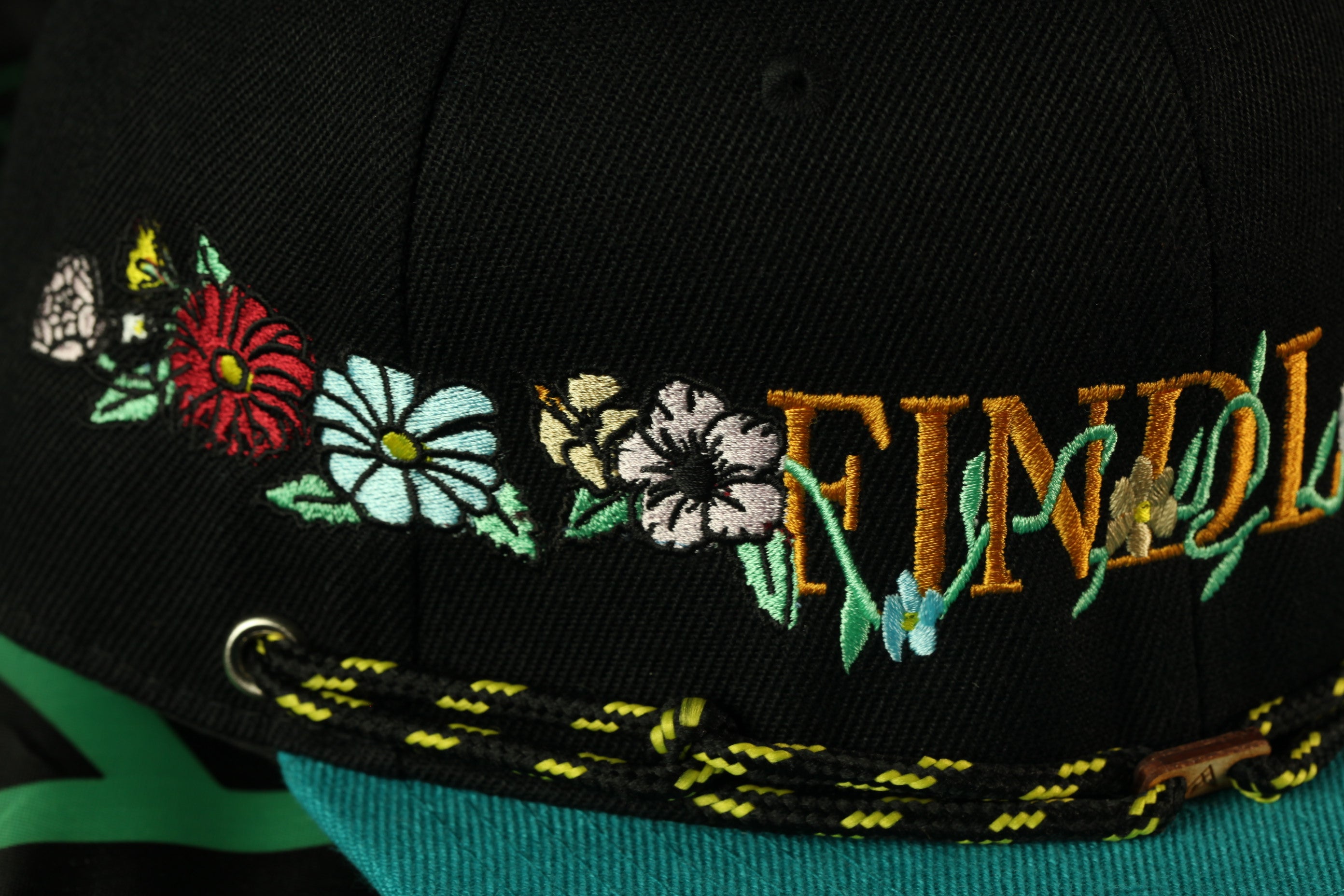 A close-up view of a black baseball cap with colorful floral embroidery and the word "FIND" written on it.