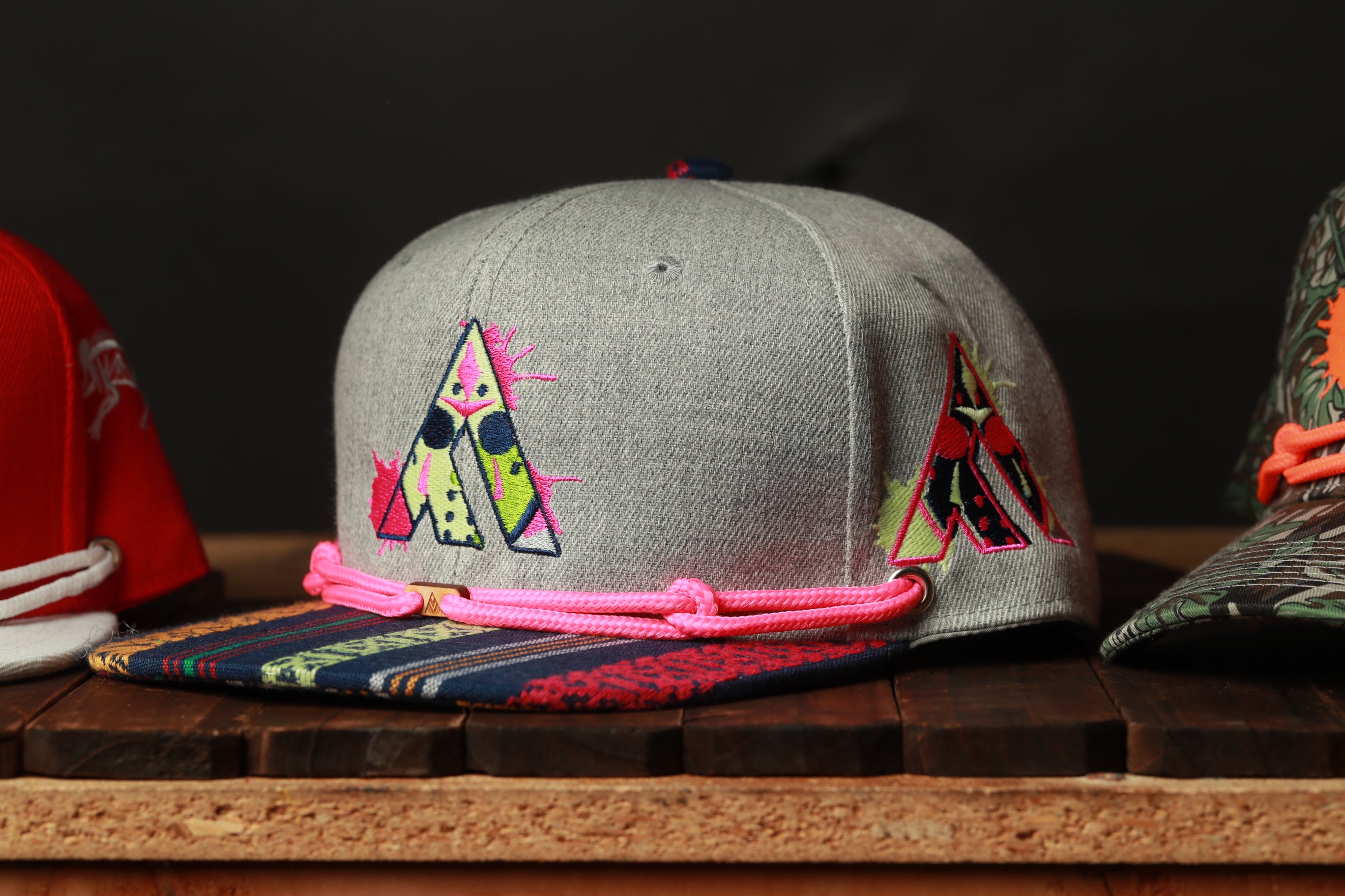 A gray baseball cap with colorful embroidered designs on it, sitting on a wooden surface.