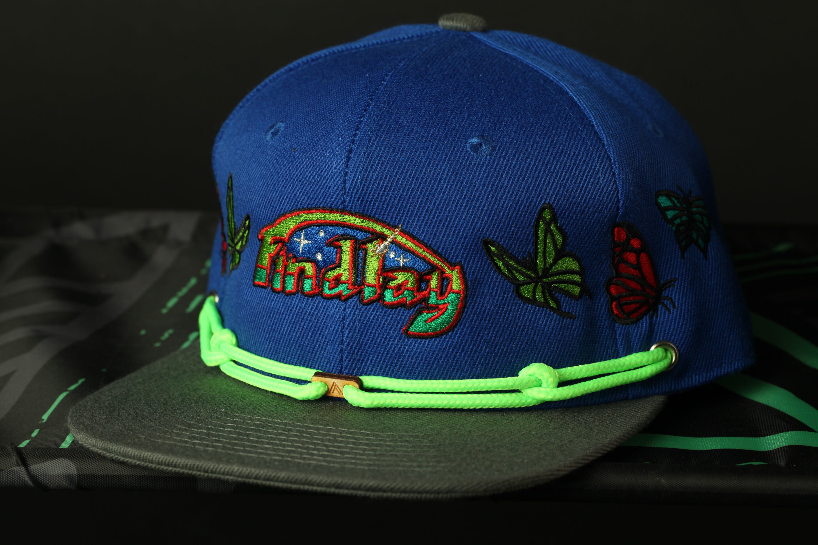 A blue baseball cap with colorful embroidered designs, including butterflies and a rainbow pattern, is shown in the image.
