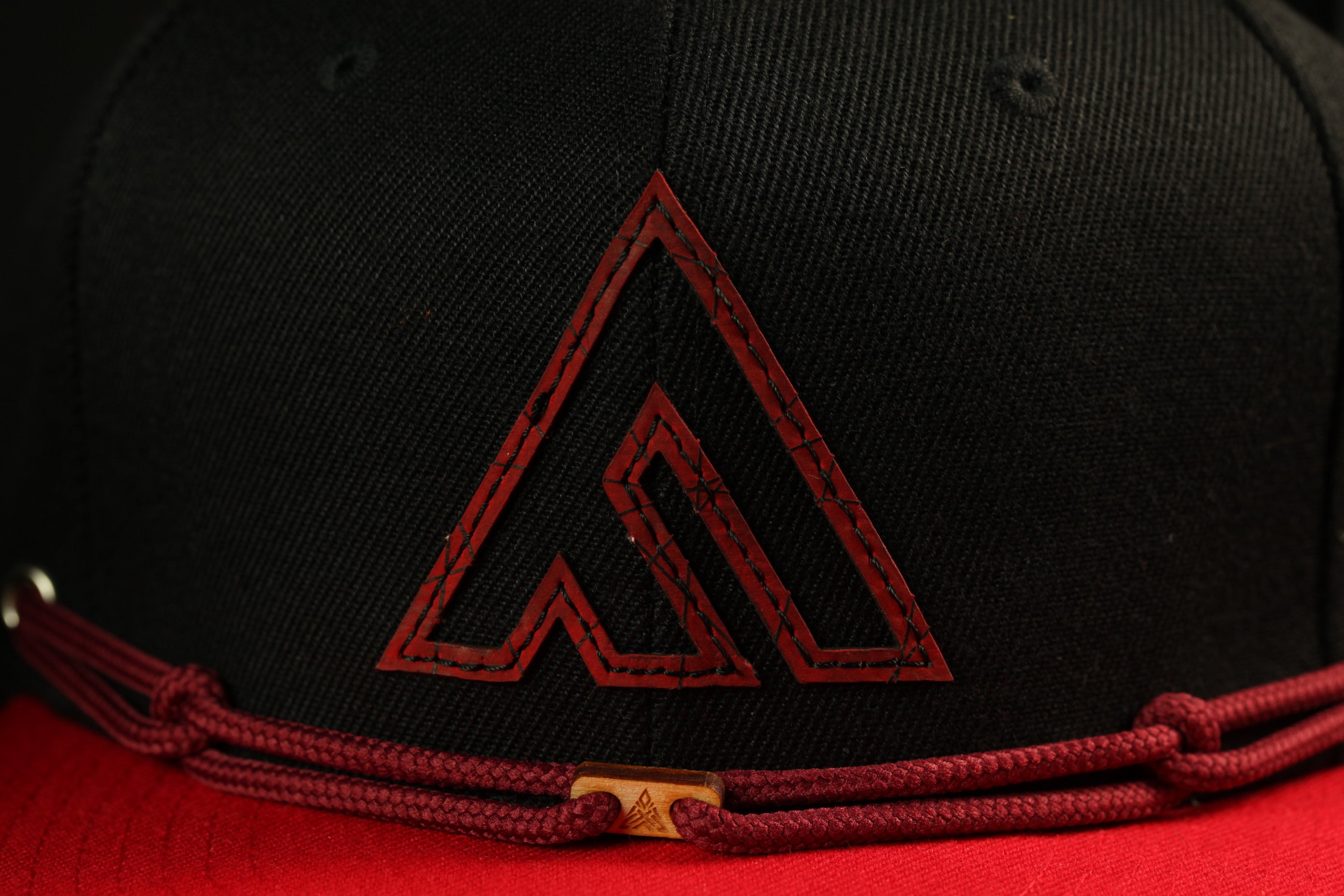 A close-up view of a black baseball cap with a red logo on the front.