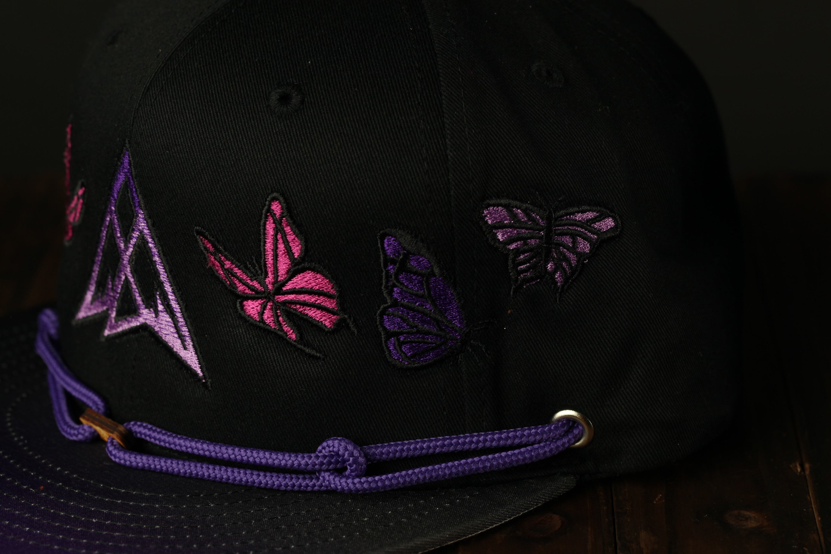 A close-up view of a black baseball cap with purple and pink butterfly embroidered designs on the front.
