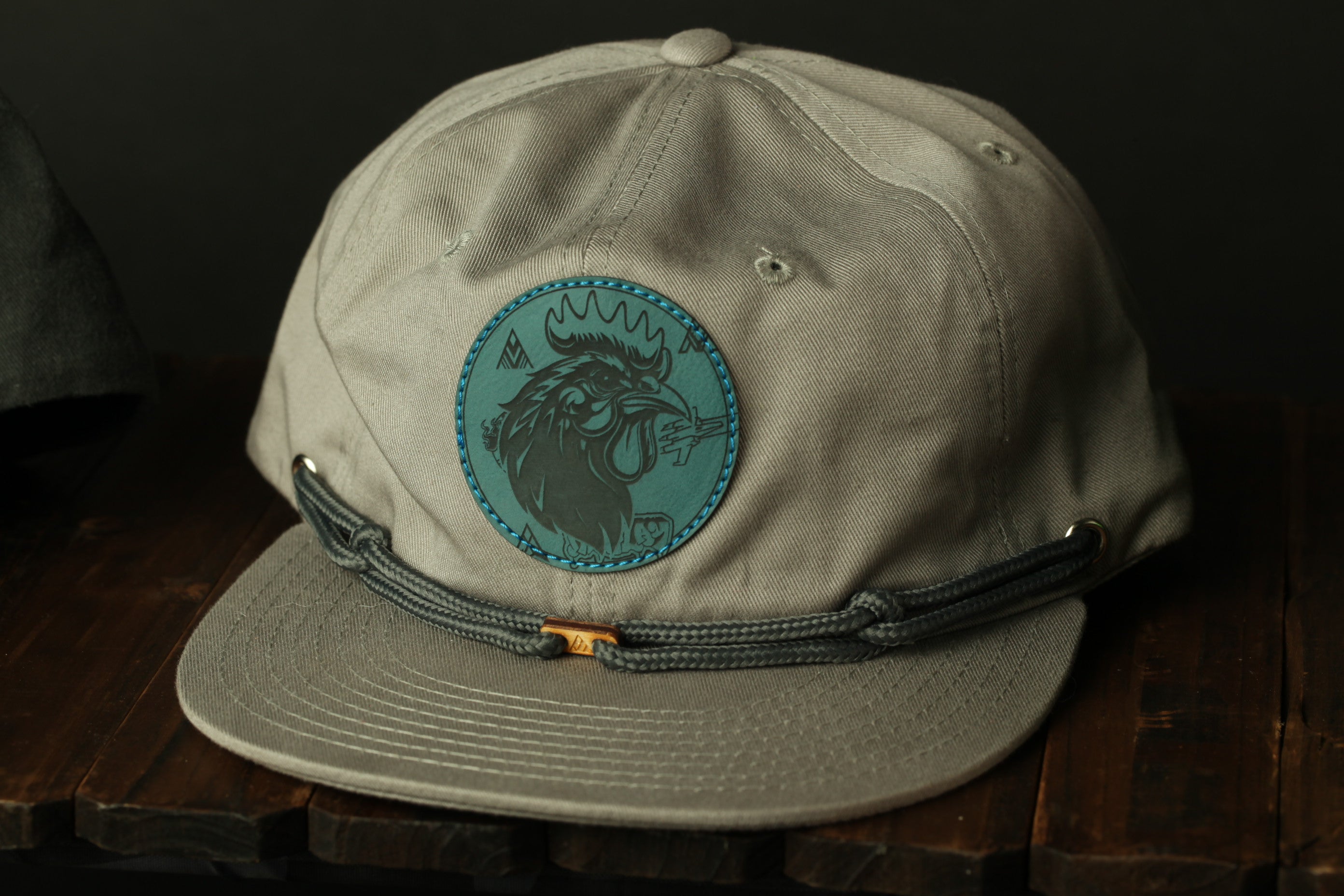 A gray baseball cap with a circular logo on the front, sitting on a wooden surface.