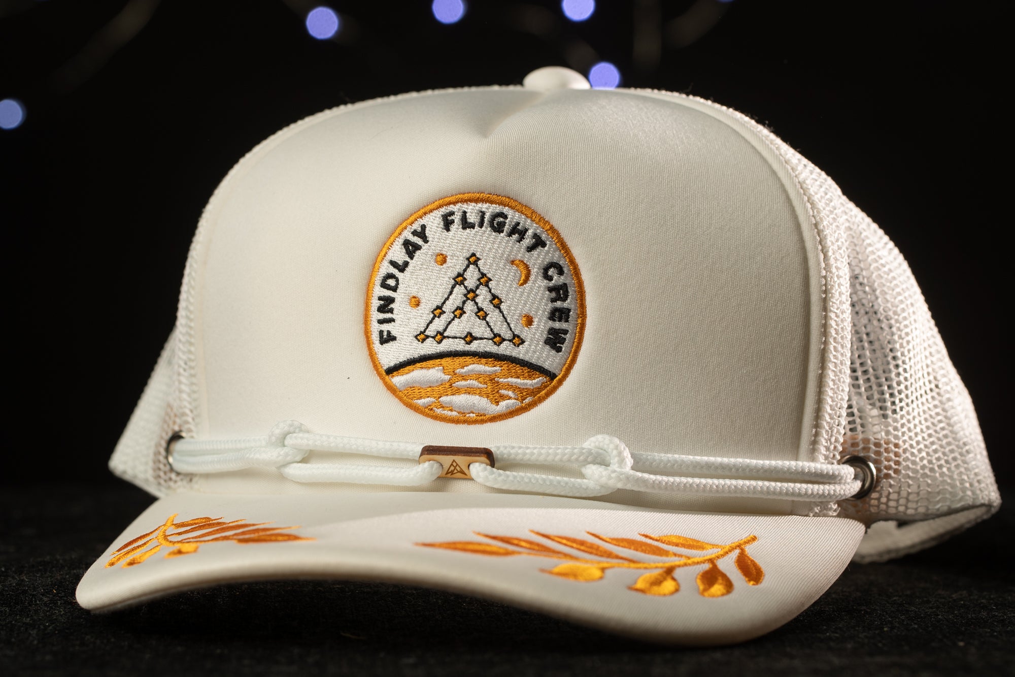 A white baseball cap with a logo on it, featuring a triangle and the text "FINDLAY FLIGHT COW" on the front.