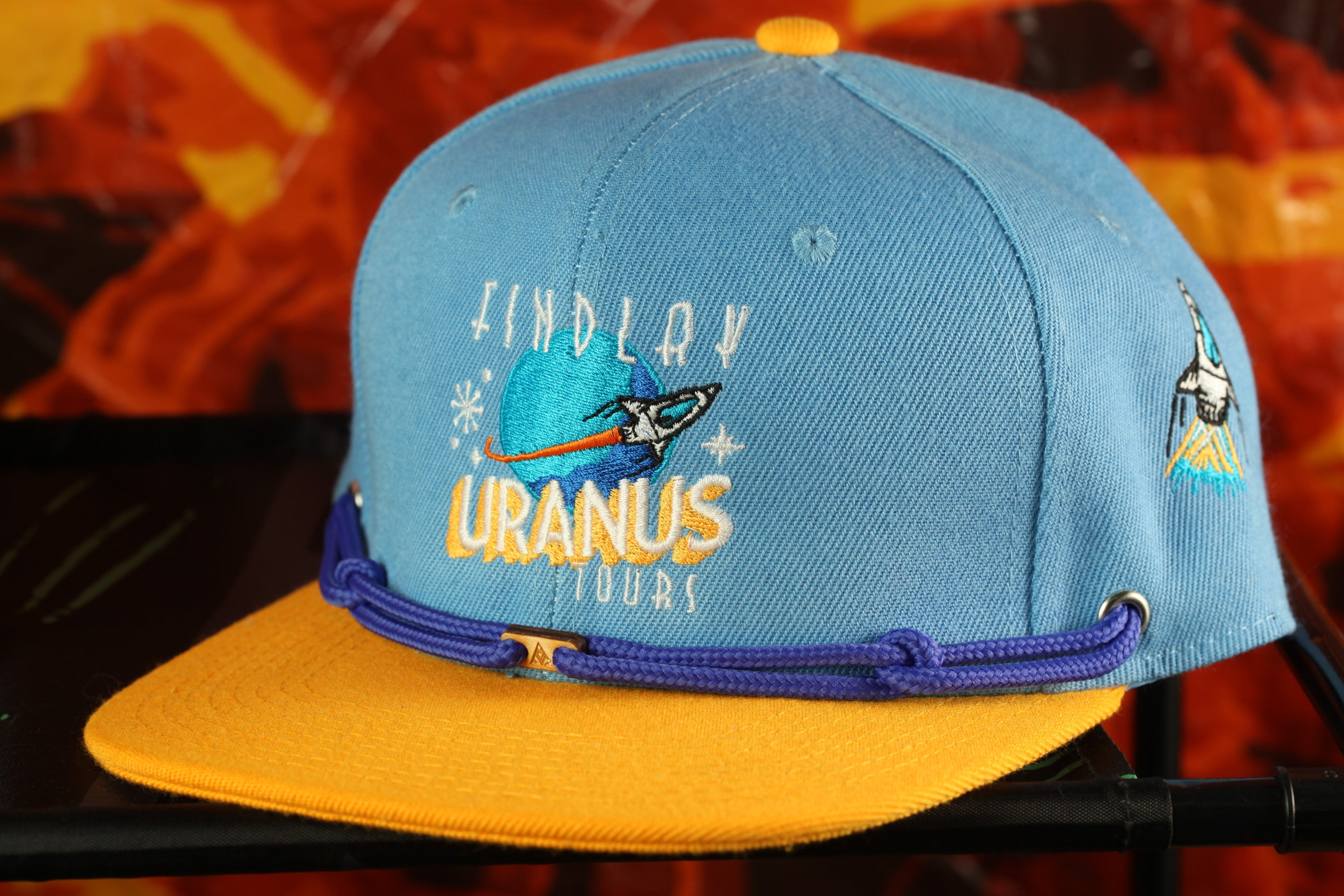 A blue baseball cap with a yellow brim and a purple string, featuring an embroidered design and text.
