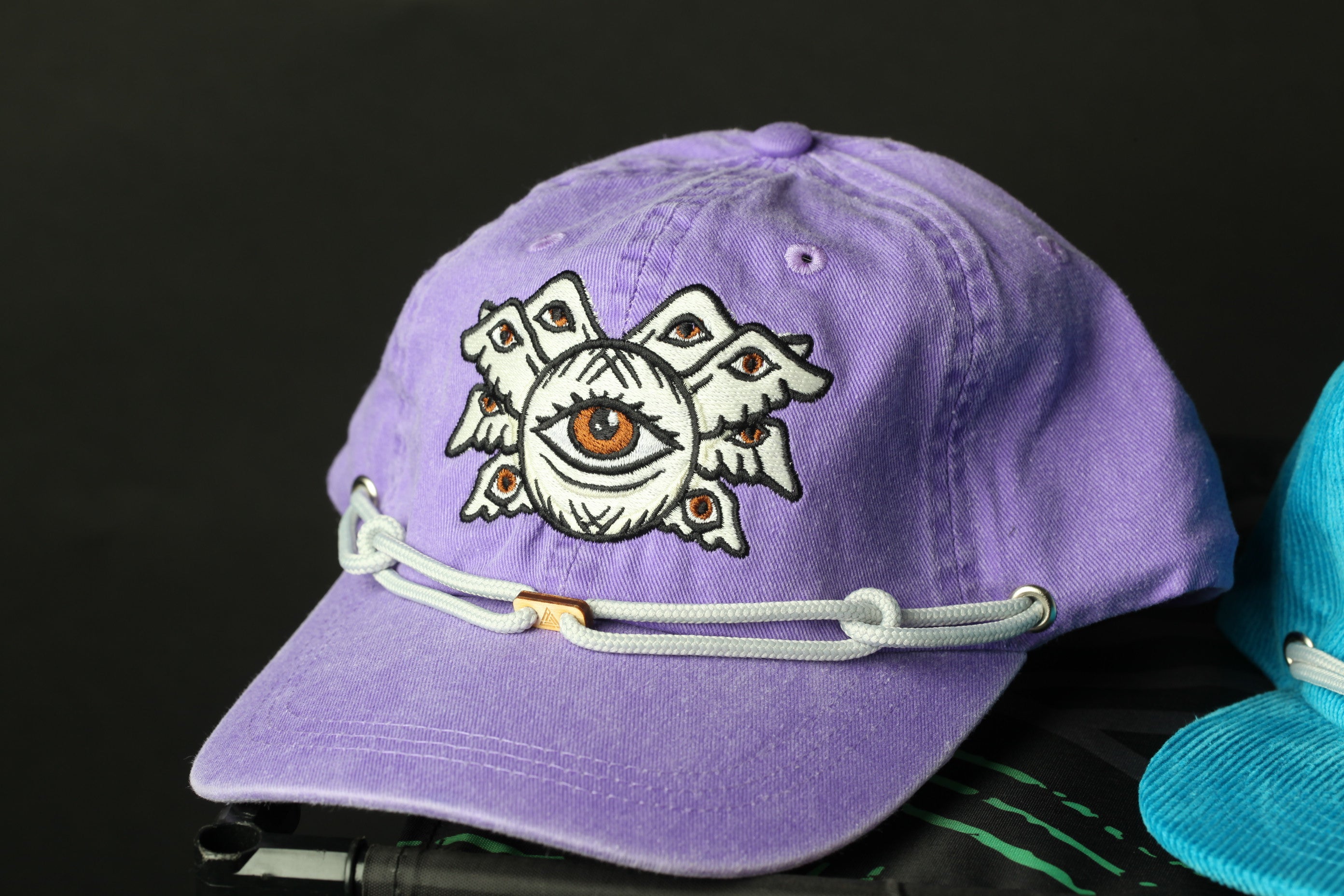 A purple baseball cap with an eye design on it, sitting on a surface.