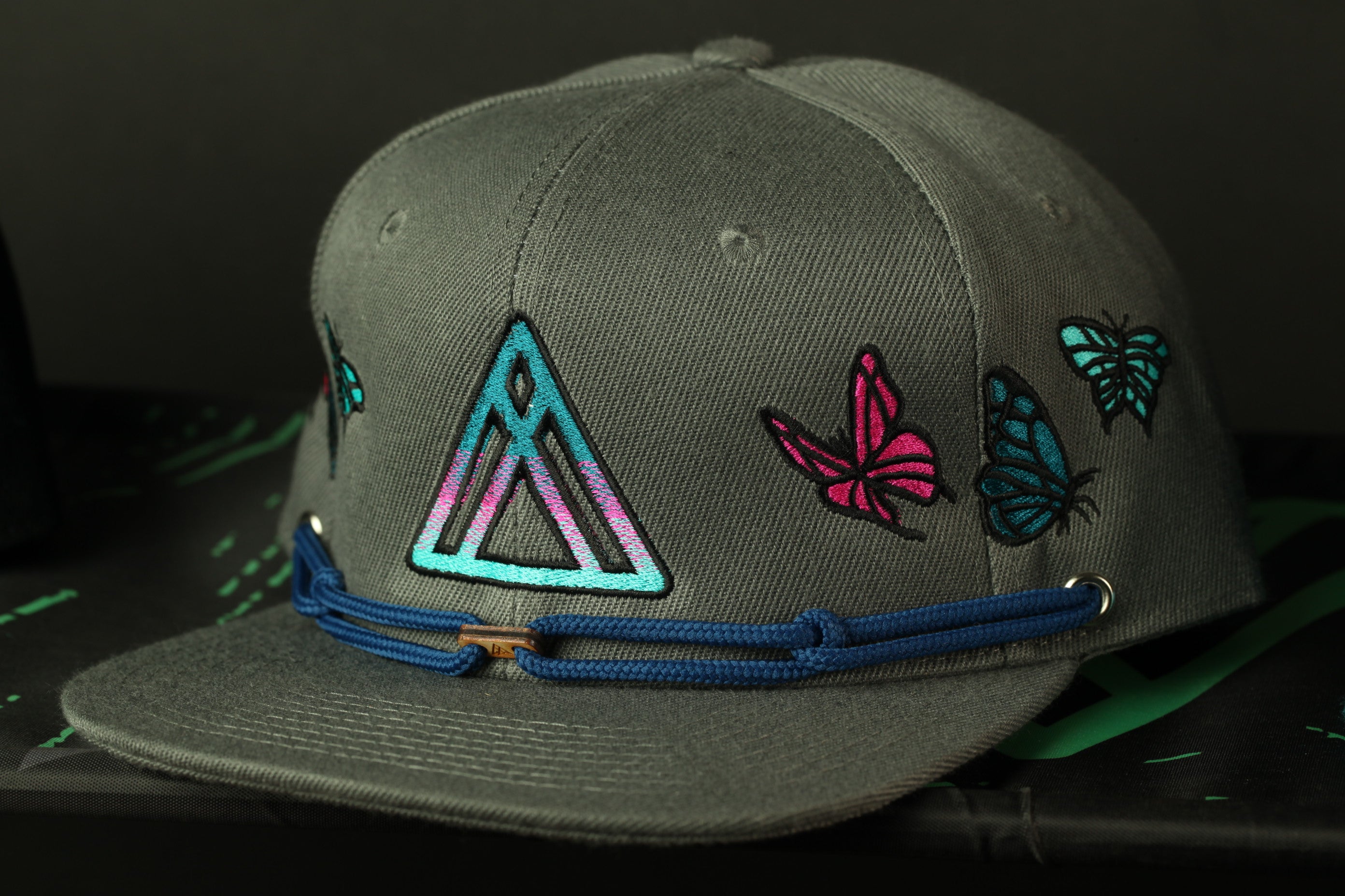 A gray baseball cap with colorful butterfly and triangle designs on the front.